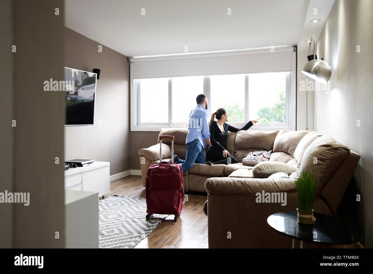 Young couple looking though window while kneeling on sofa in rental house Stock Photo