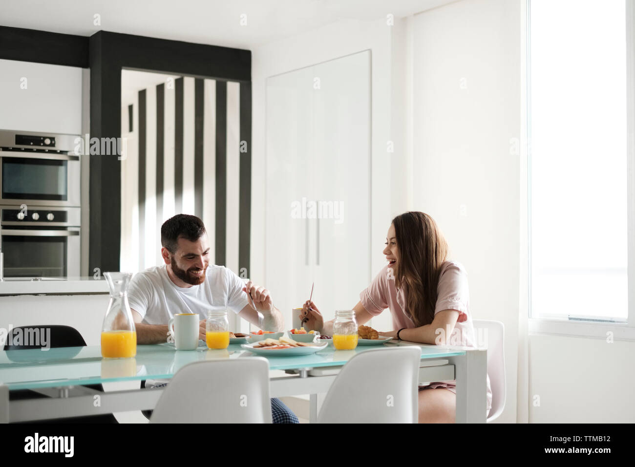 Happy young couple having breakfast at dining table in rental house Stock Photo