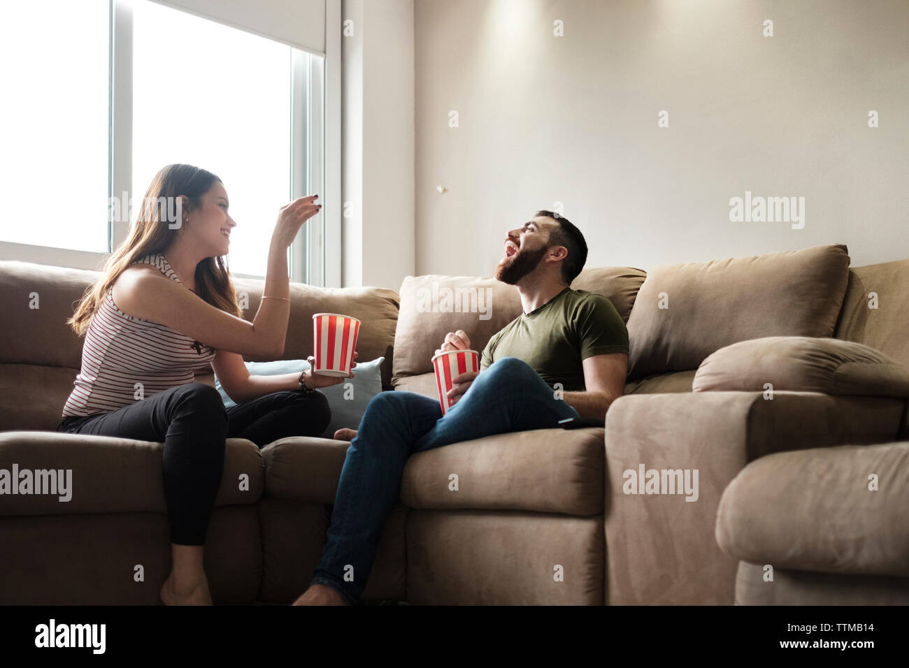 Playful girlfriend throwing popcorn in boyfriend's mouth while sitting