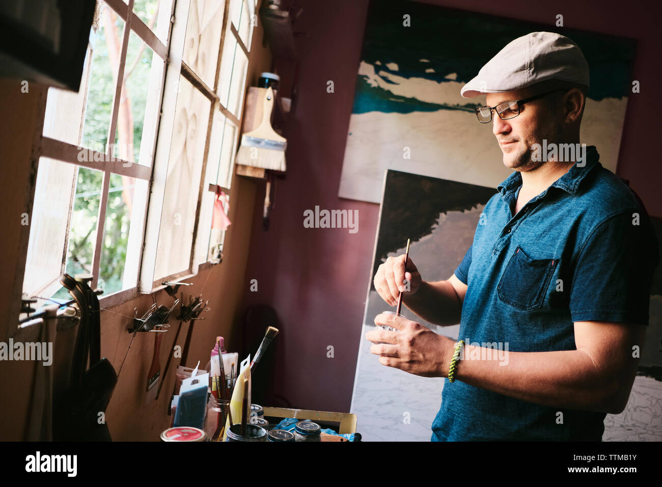Mid adult male Cuban artist mixing paint with brush in his workshop Stock Photo