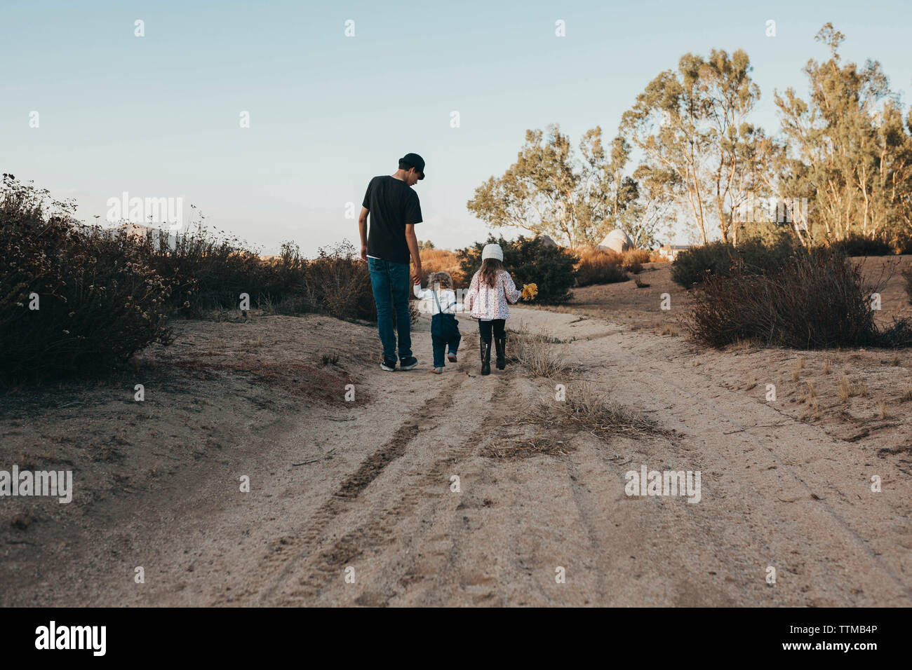 Rear view of siblings walking on ground against sky Stock Photo