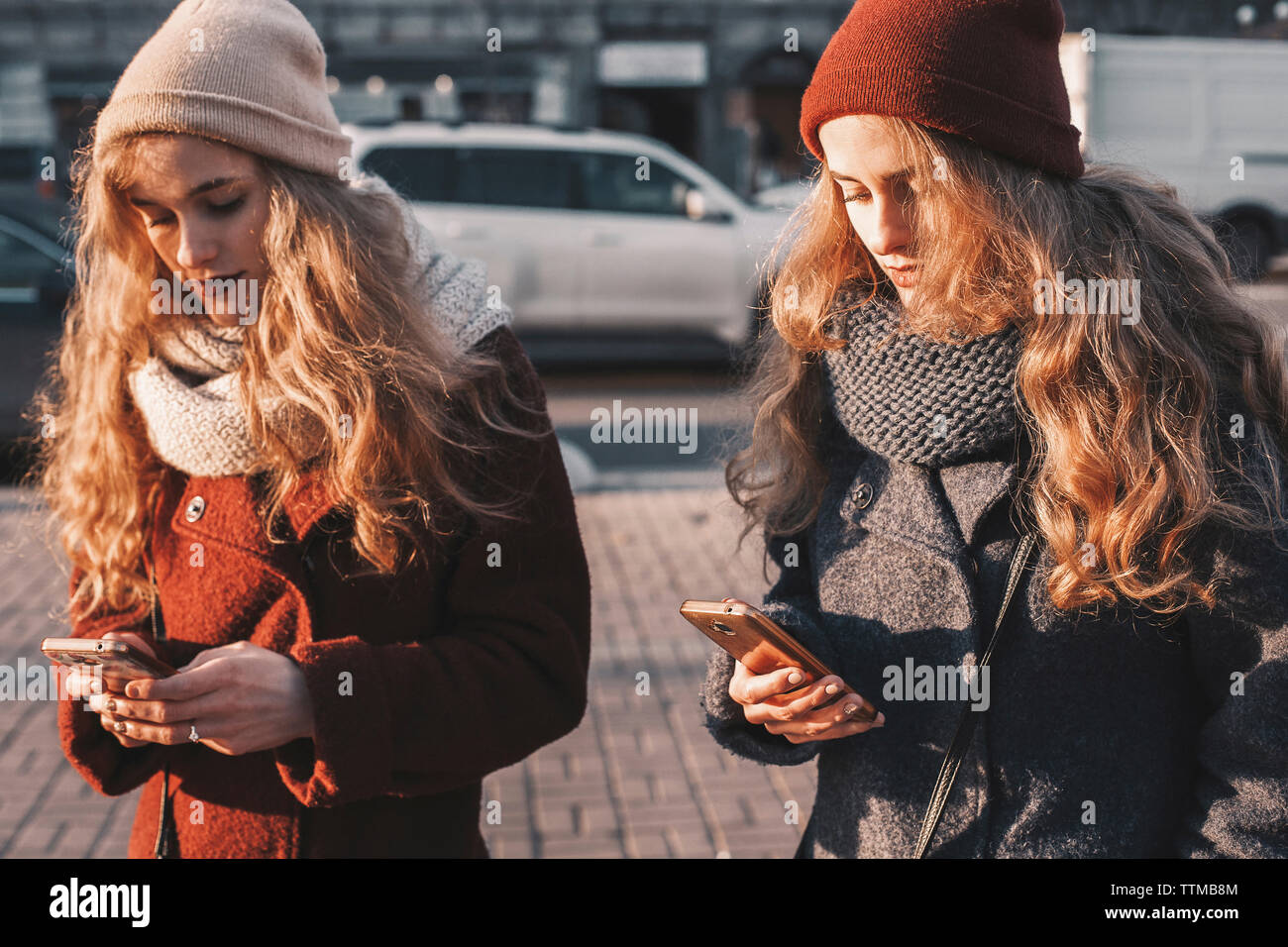 Sisters using mobile phones while standing on city street Stock Photo