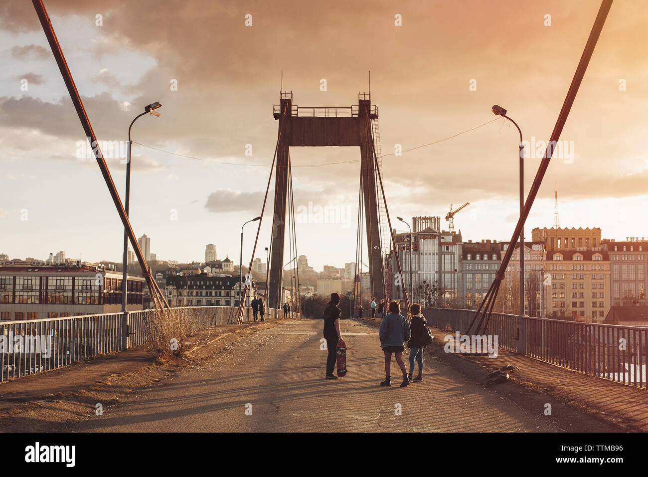 Friends walking on bridge against cloudy sky during sunset Stock Photo