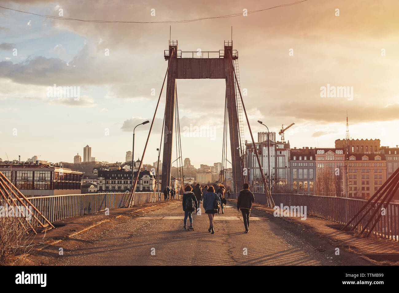 Rear view of friends walking on bridge against cloudy sky during sunset Stock Photo