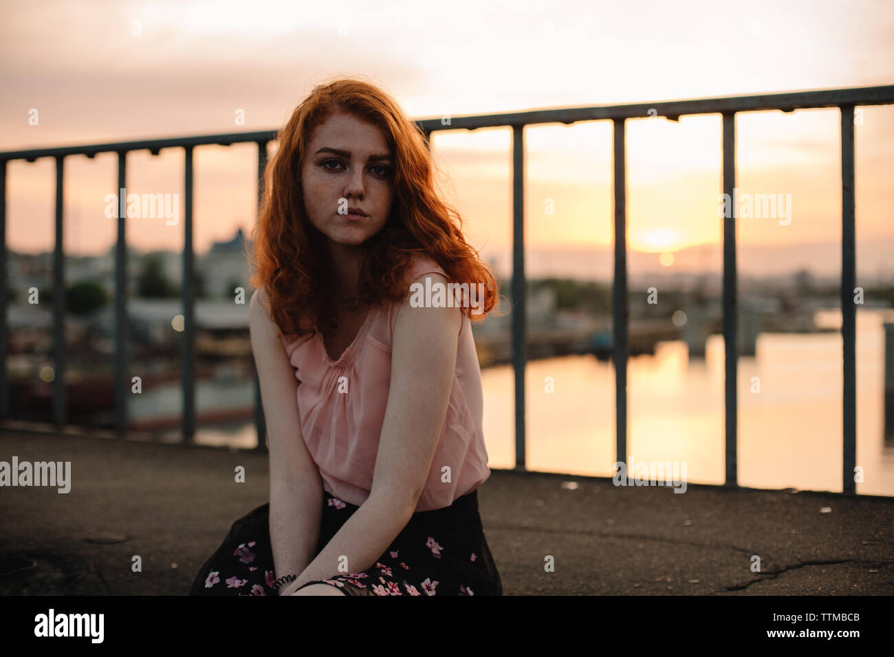 Portrait of young woman with red hair sitting on bridge at sunset Stock ...
