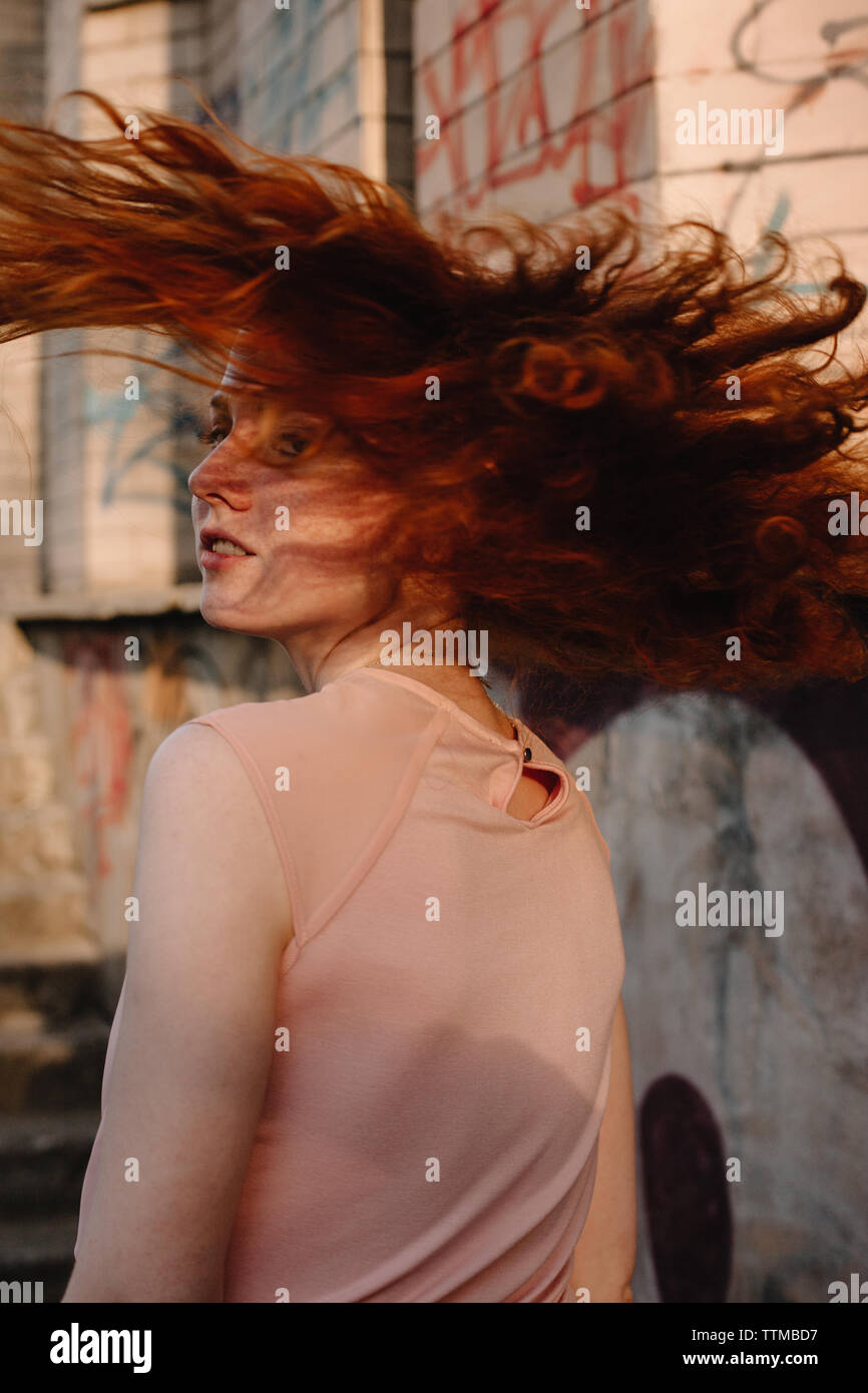 Redheaded teenager tossing hair while walking in city street Stock Photo