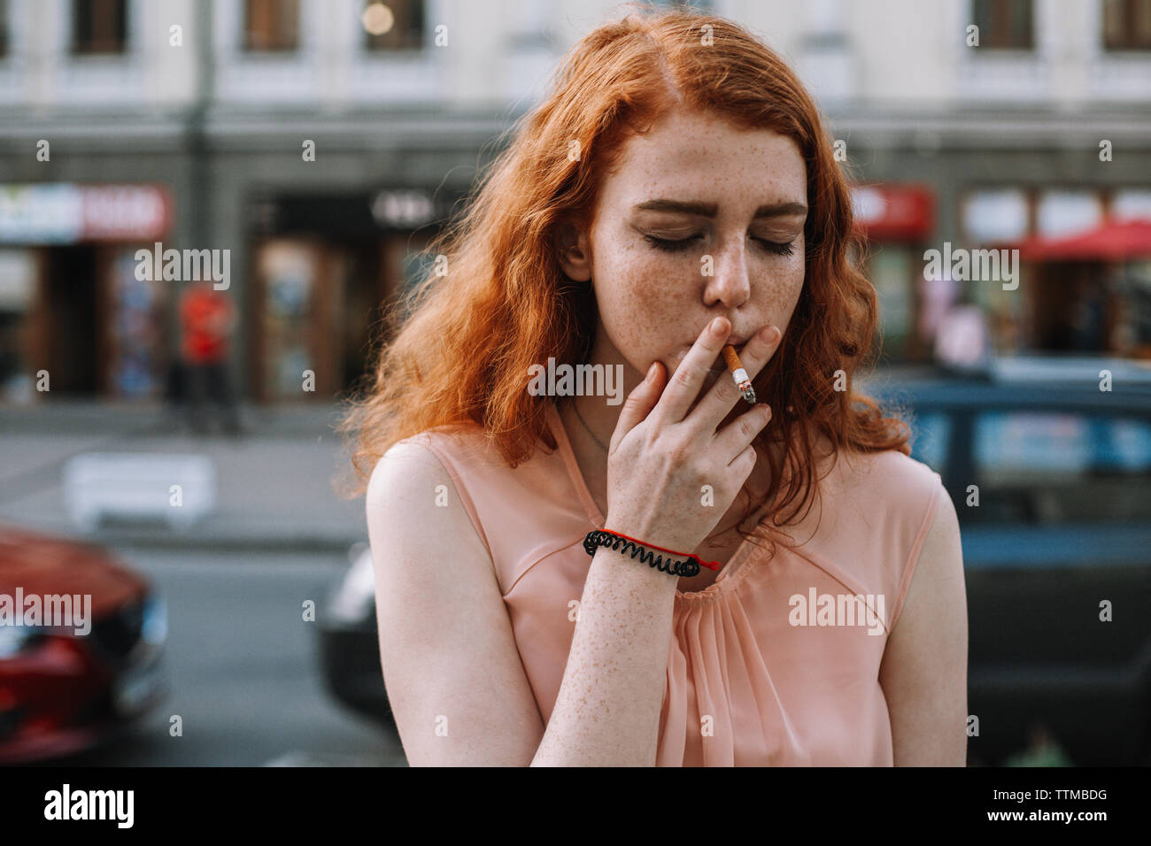 Young woman with freckles smoking cigarette while standing in street Stock Photo