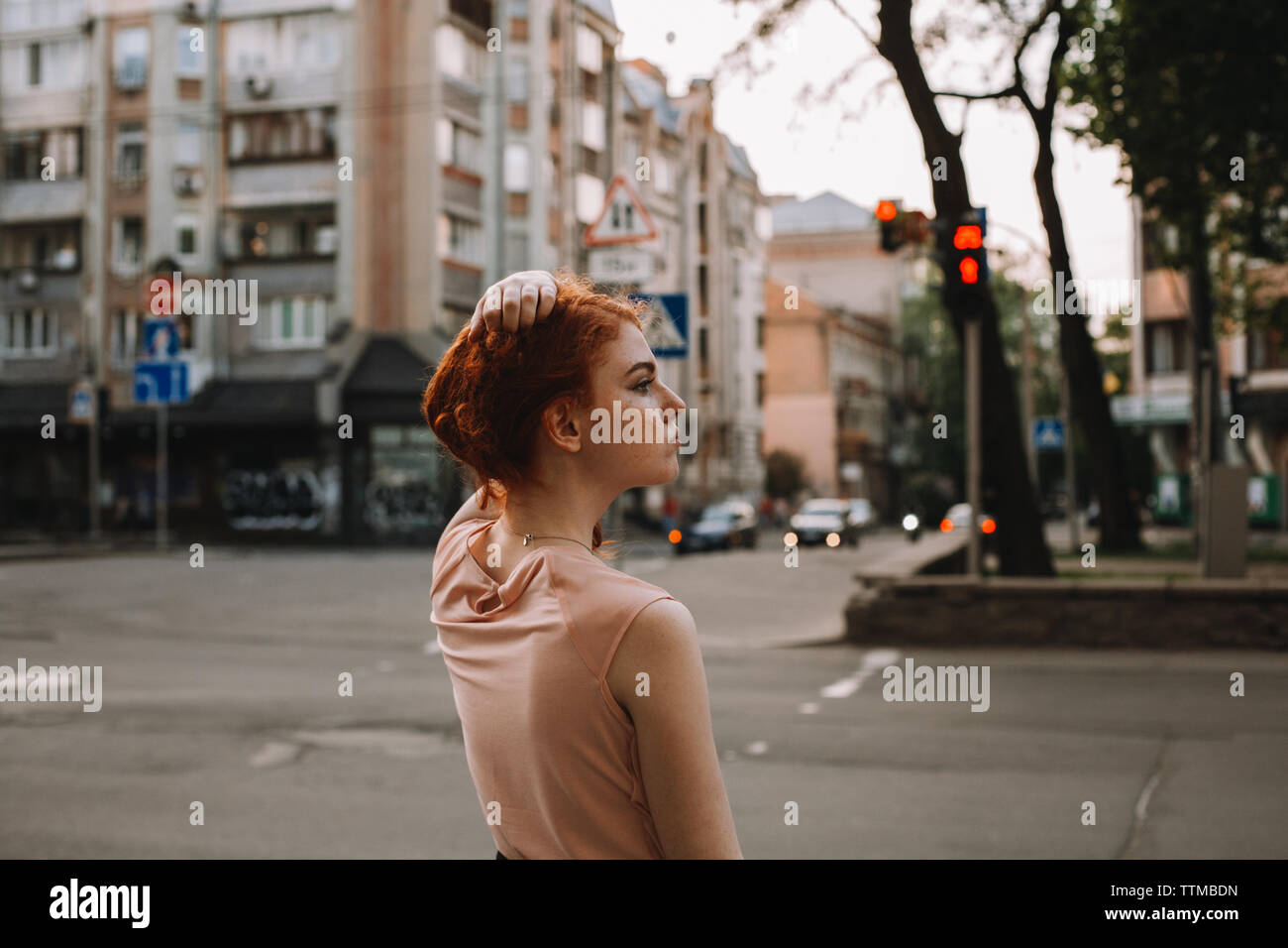 Young redheaded woman holding hair while standing in city street Stock Photo