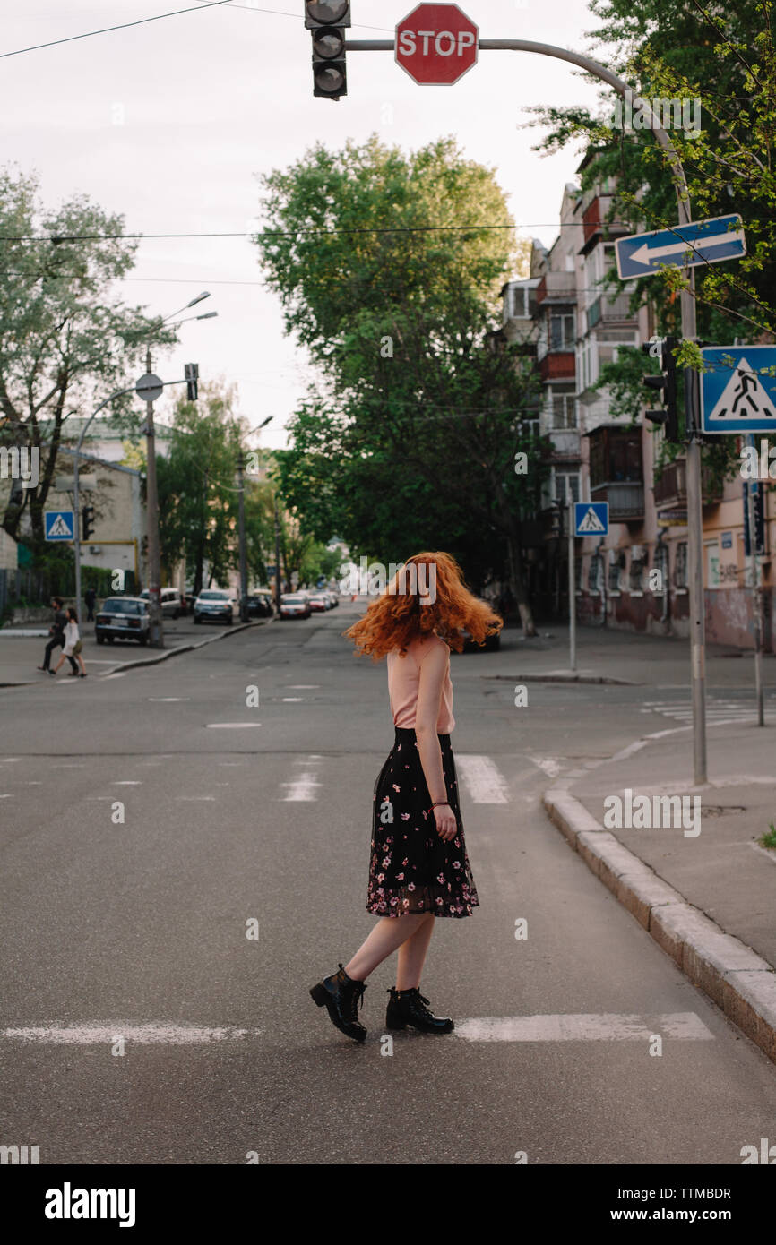 Redheaded woman tossing hair while crossing road in city Stock Photo