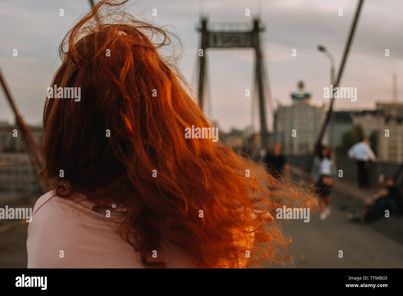 Rear view of woman with red hair walking on bridge in city Stock Photo