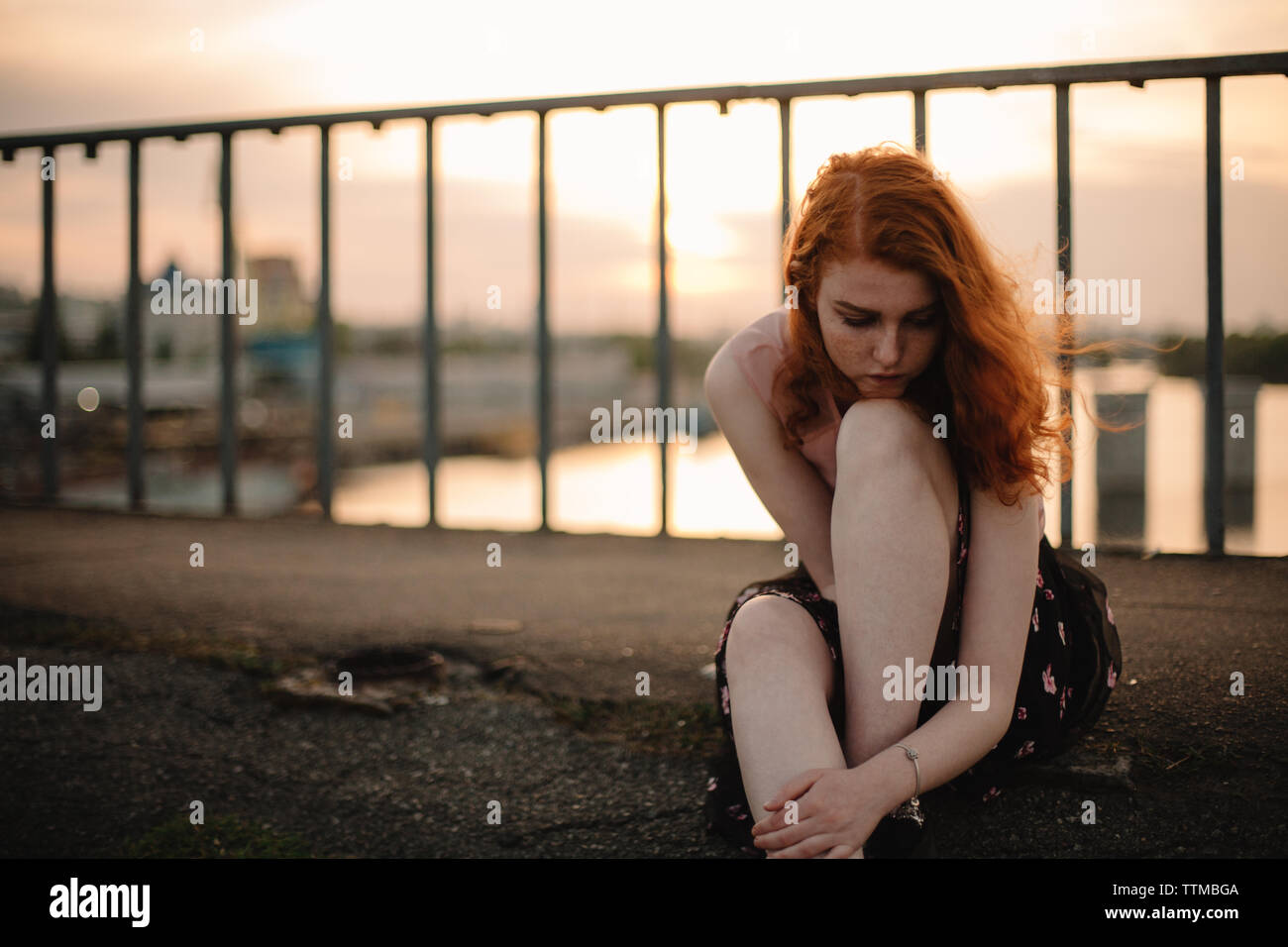 Portrait of thoughtful teenage girl sitting on bridge at sunset Stock Photo