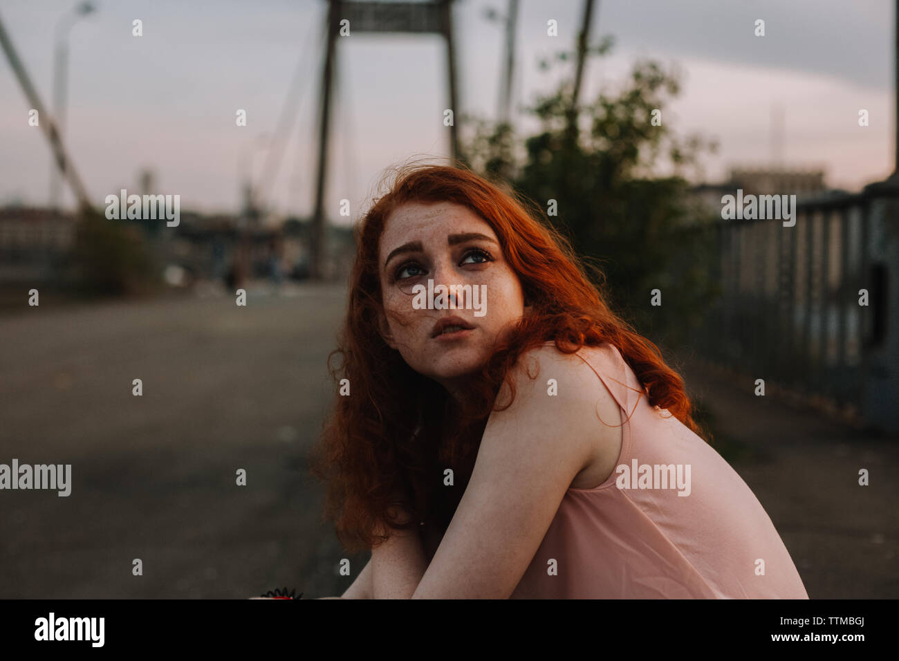 Portrait of teenage girl with freckles sitting on bridge in city Stock Photo