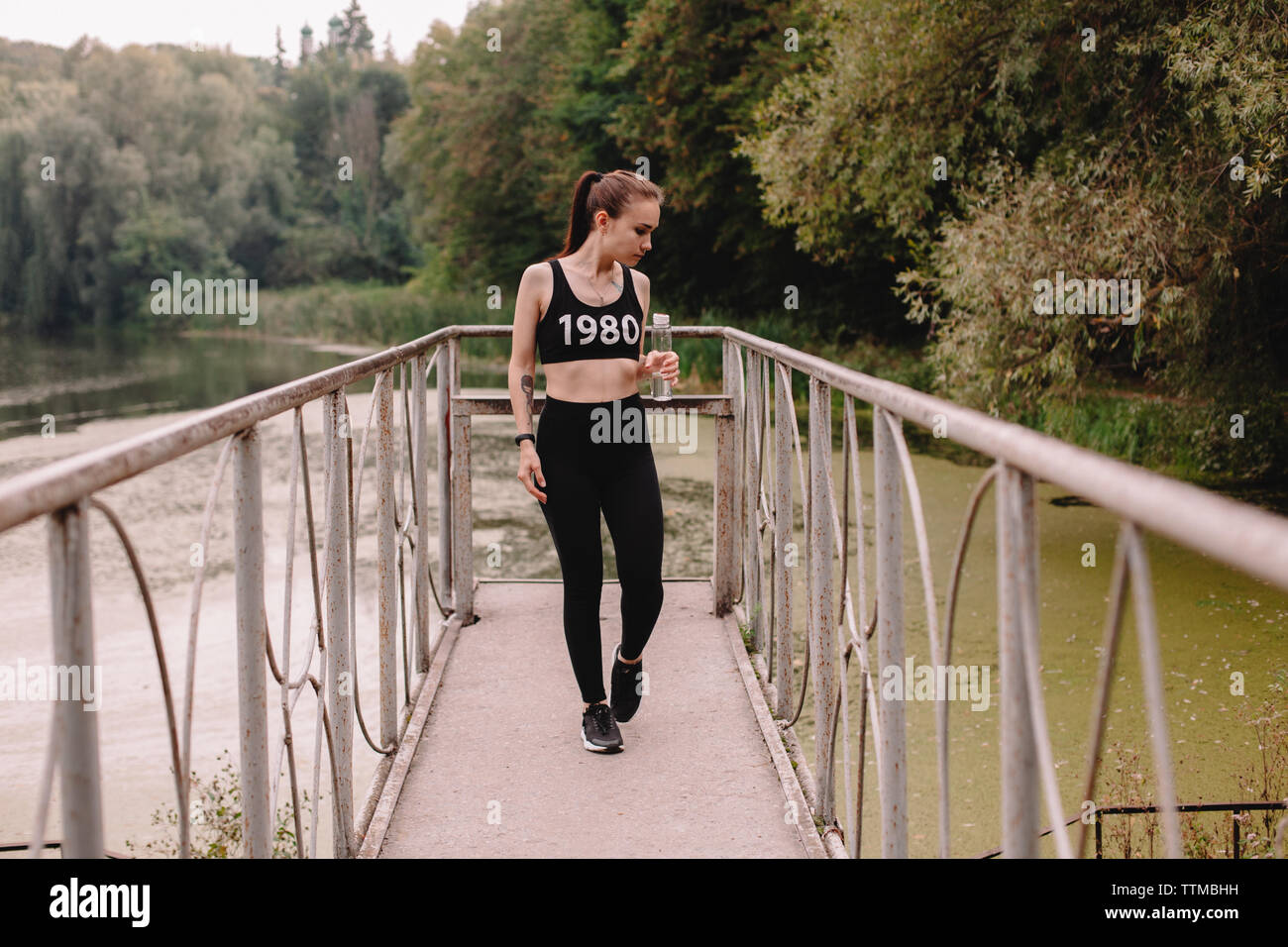 Female jogger walking on pier by lake in park Stock Photo