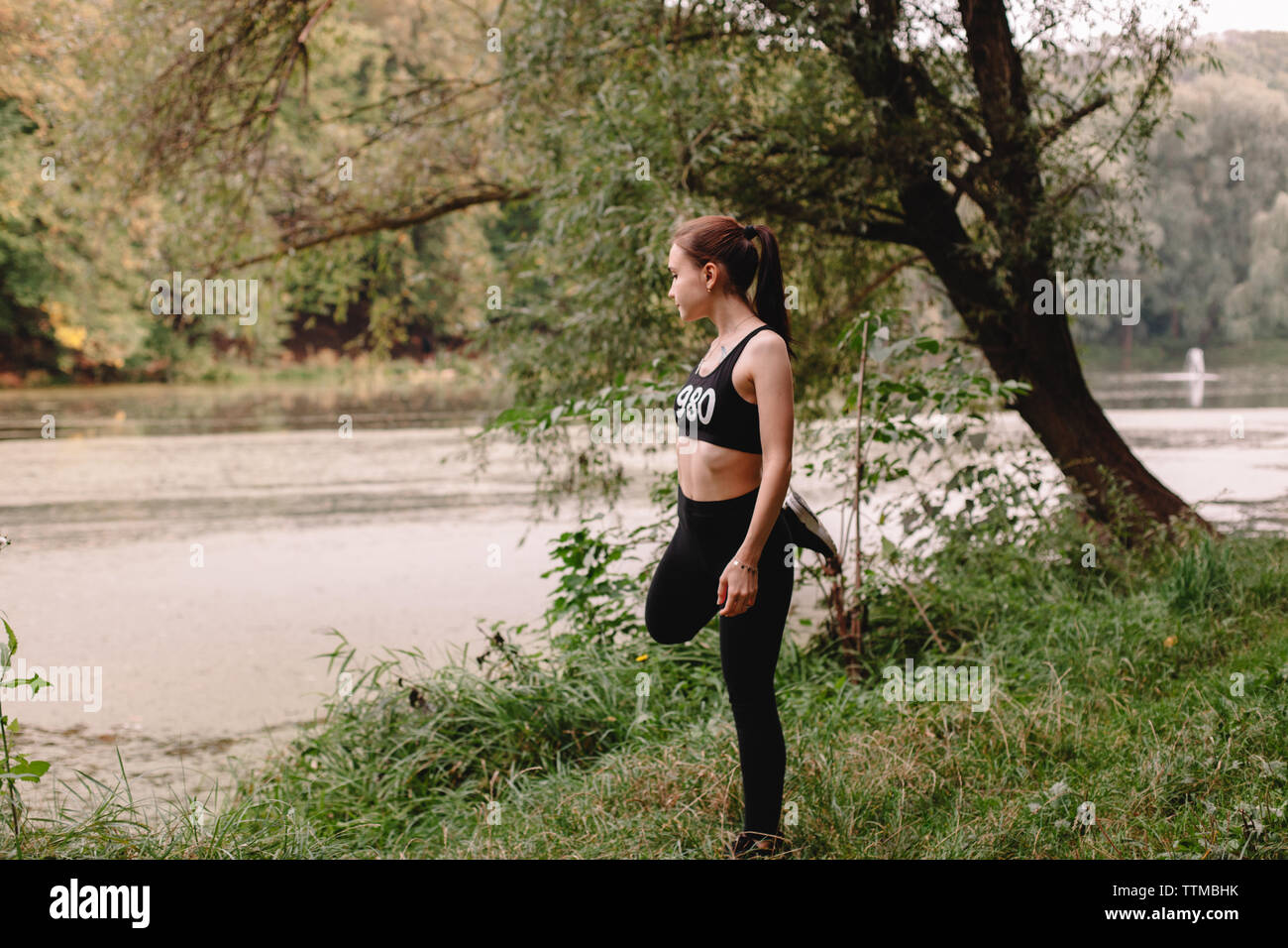 Female jogger stretching by lake in park Stock Photo