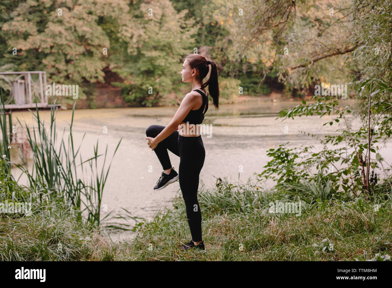 Side view of female jogger stretching at lakeshore in park Stock Photo