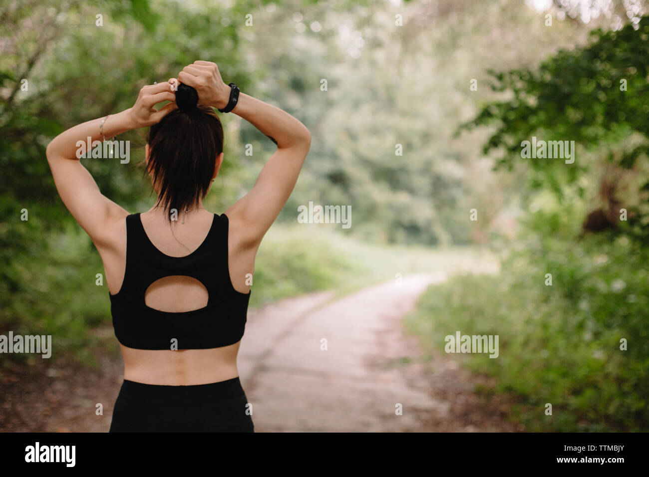 Rear view of female jogger making hair bun at park Stock Photo