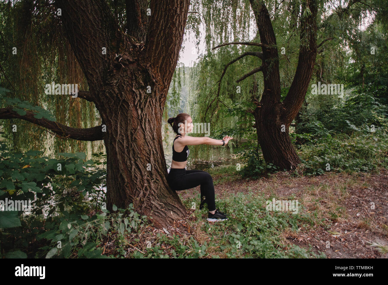 Sporty woman exercising by tree at lakeshore in park Stock Photo - Alamy