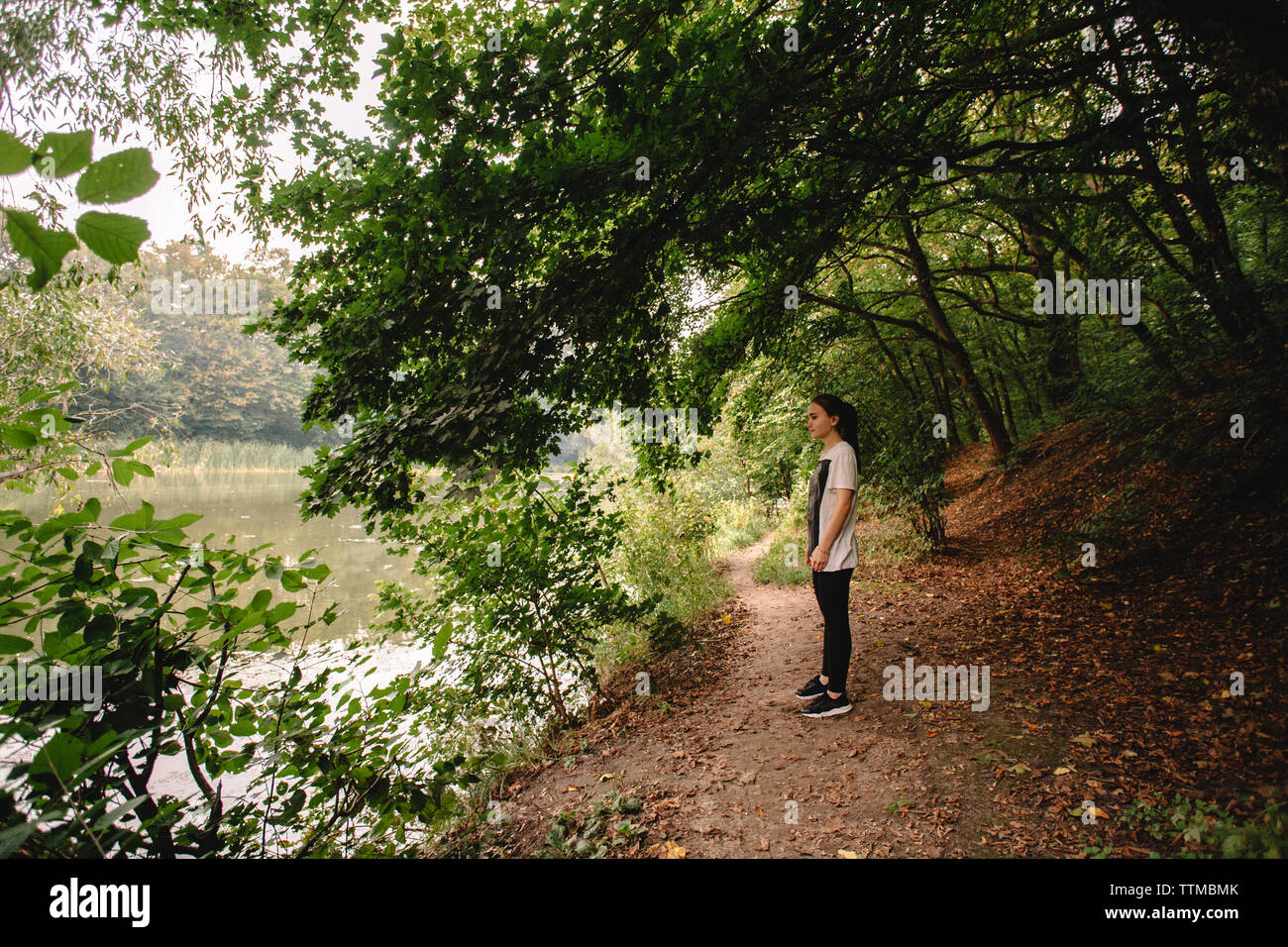 Side view of woman looking at lake while standing at lakeshore Stock Side view of woman looking at lake while standing at lakeshore Stock