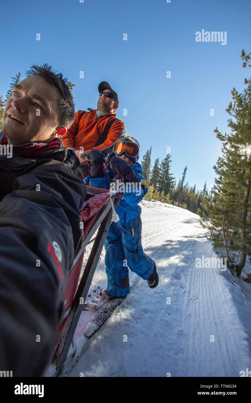 USA, Oregon, Bend, a young boy stands with the musher on the footboards while being pulled around Mt. Bachelor by the sled dogs Stock Photo