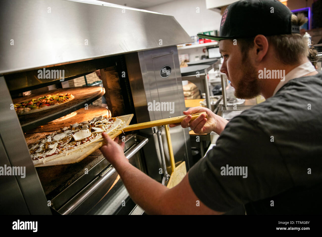 USA, Oregon, Bend, Pacific Pizza and Brew, man putting pizza in oven Stock Photo