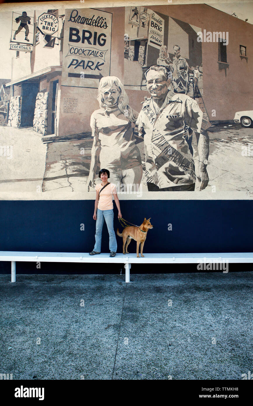 USA, Los Angeles, a woman standing in front of a wall mural on the side of a building on Abbot Kinney Boulevard with her dog Stock Photo