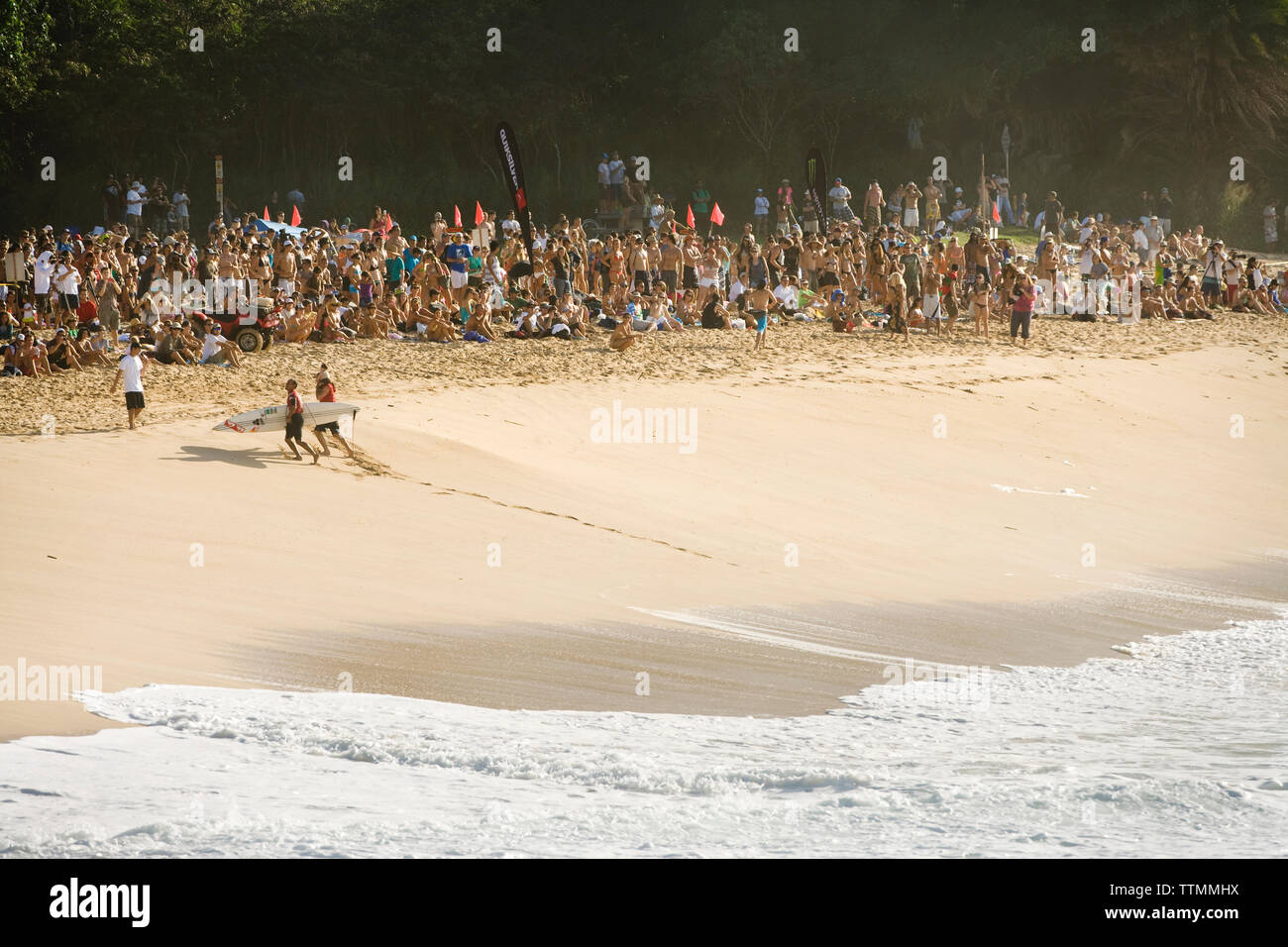 USA, Hawaii, crowd watches Ramon Navarro run up the beach after surfing a huge wave, Waimea Bay, Oahu Stock Photo
