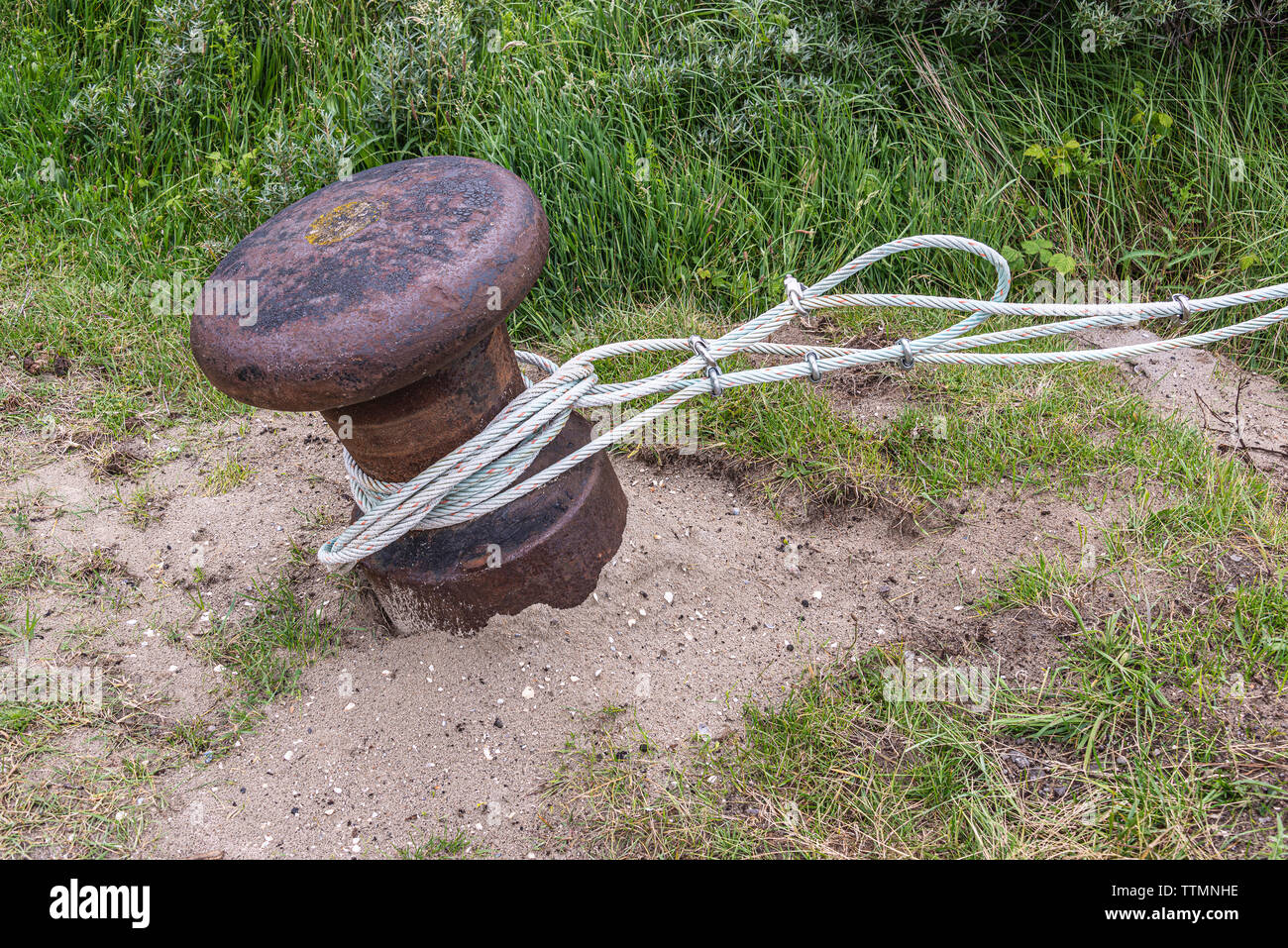 rope cable wrapped around a rusty bollard in the dune area Stock Photo