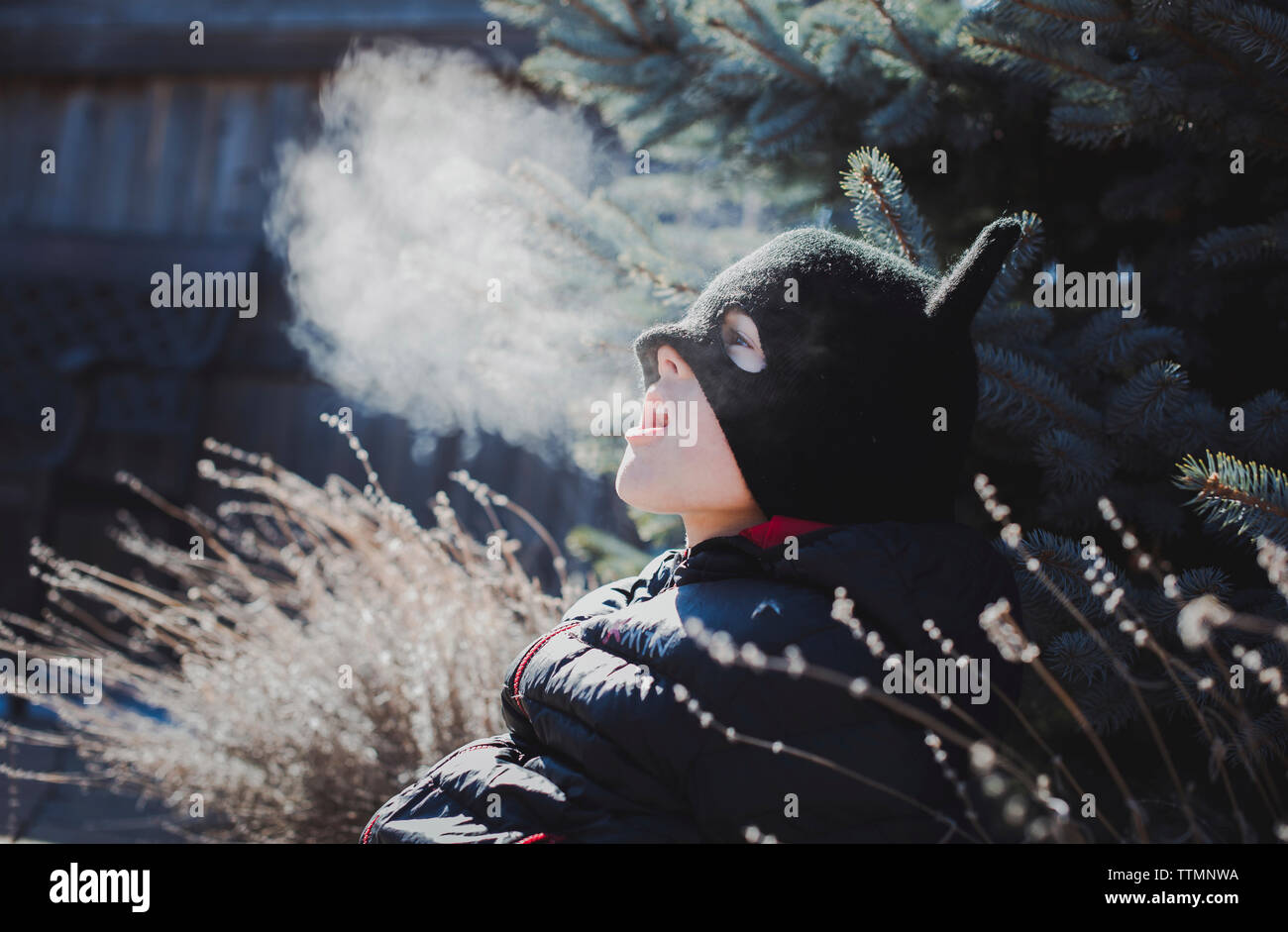 Playful boy wearing knit hat while exhaling breath vapor at yard Stock Photo