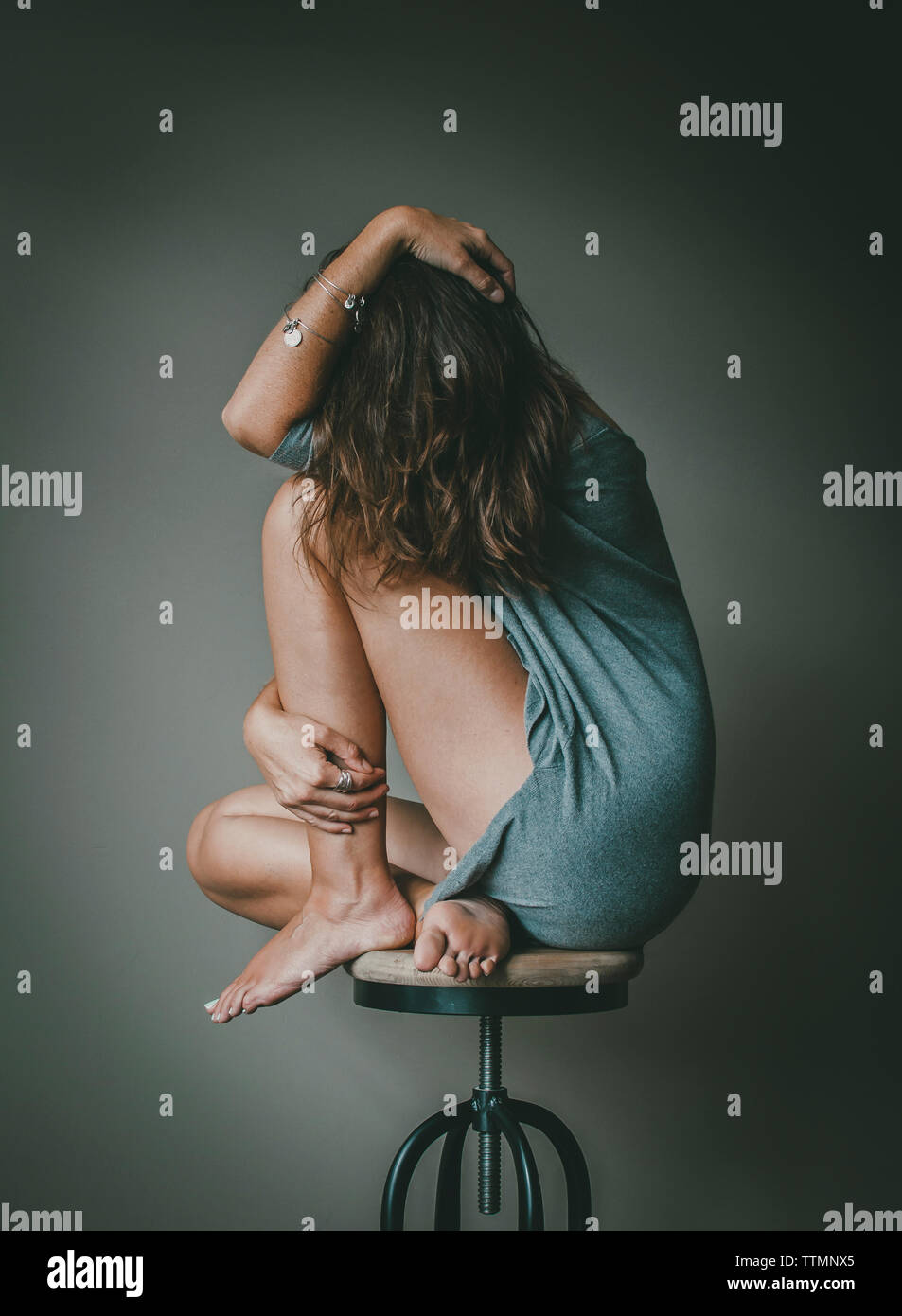 Full length of depressed woman with obscured face sitting on stool against wall Stock Photo
