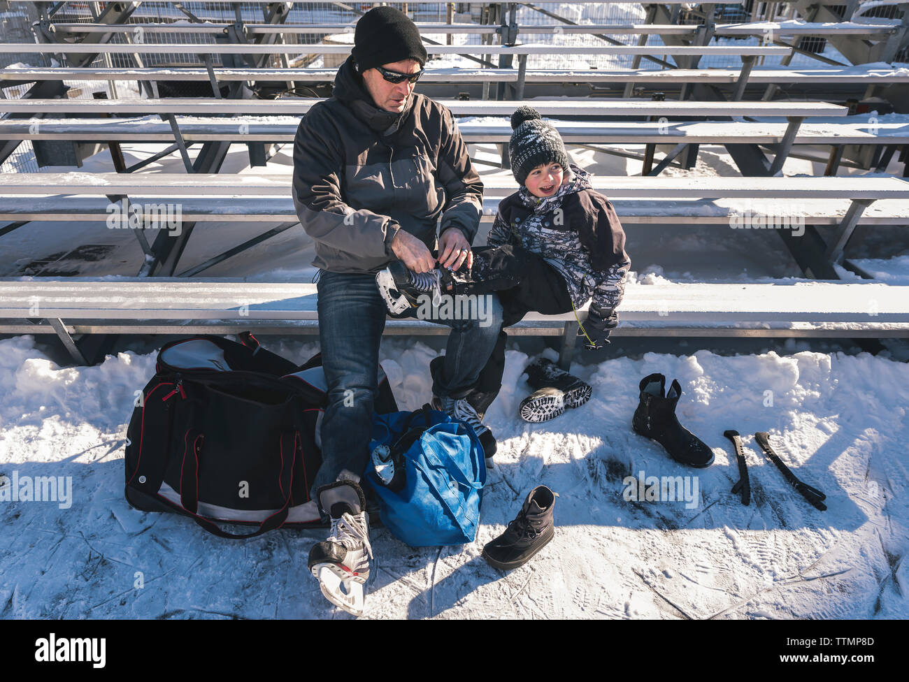 High angle view of father tying son's shoelace while sitting on bench during winter Stock Photo
