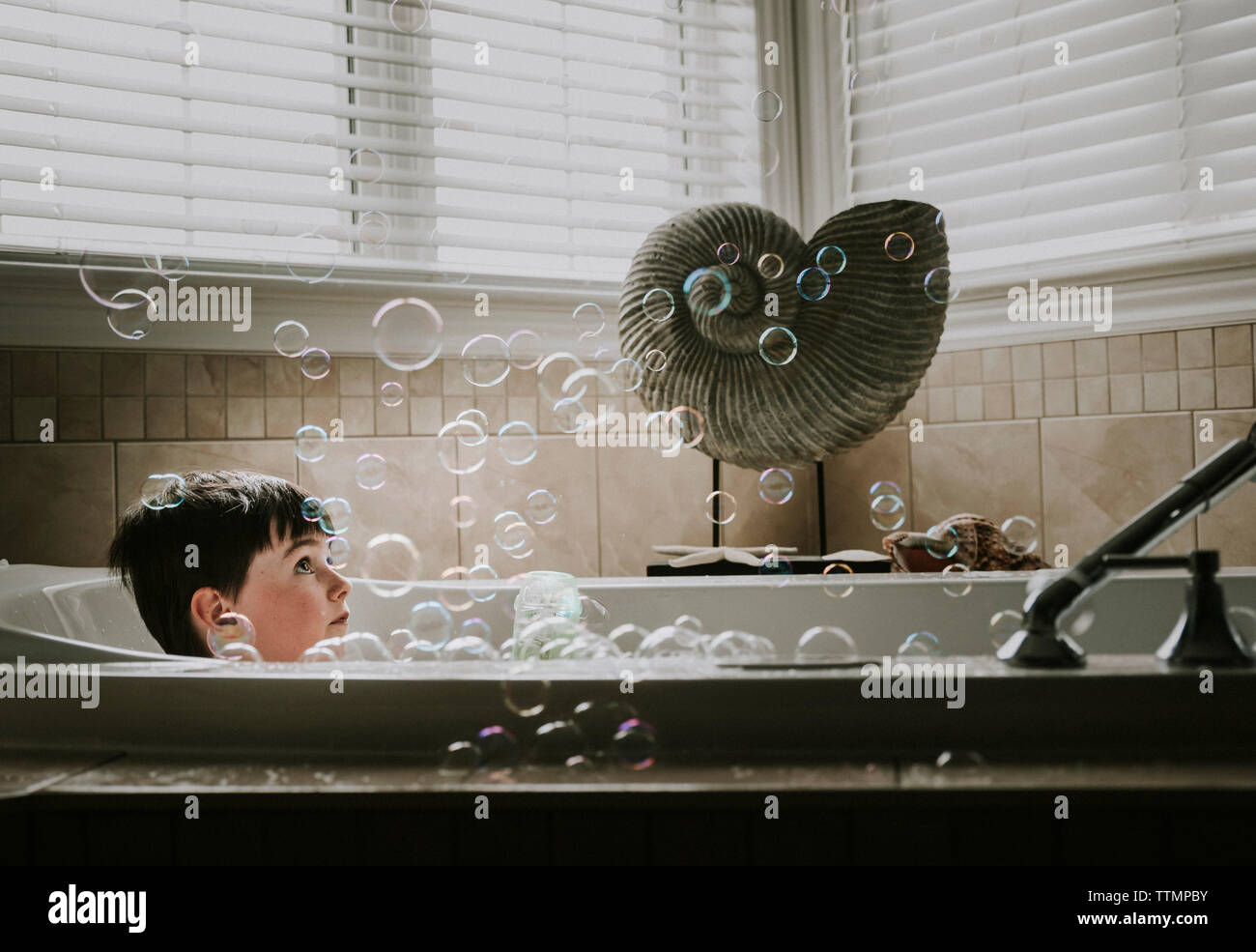 Boy looking at bubbles while taking bath in bathtub Stock Photo