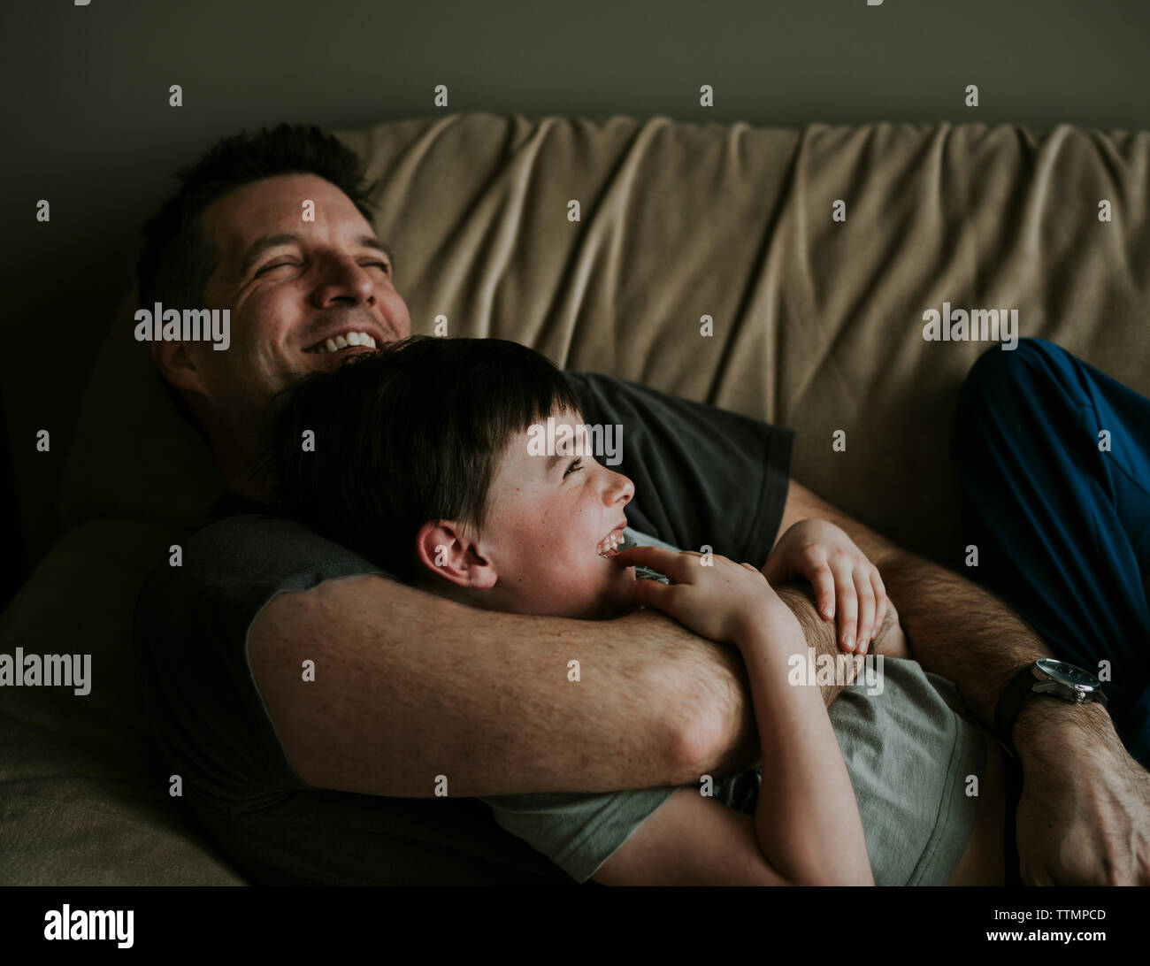 Happy father embracing son while lying on sofa at home Stock Photo