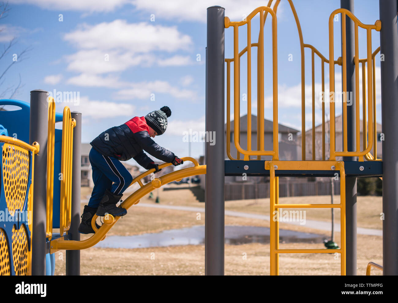 Side view of boy climbing ladder against sky at playground Stock Photo