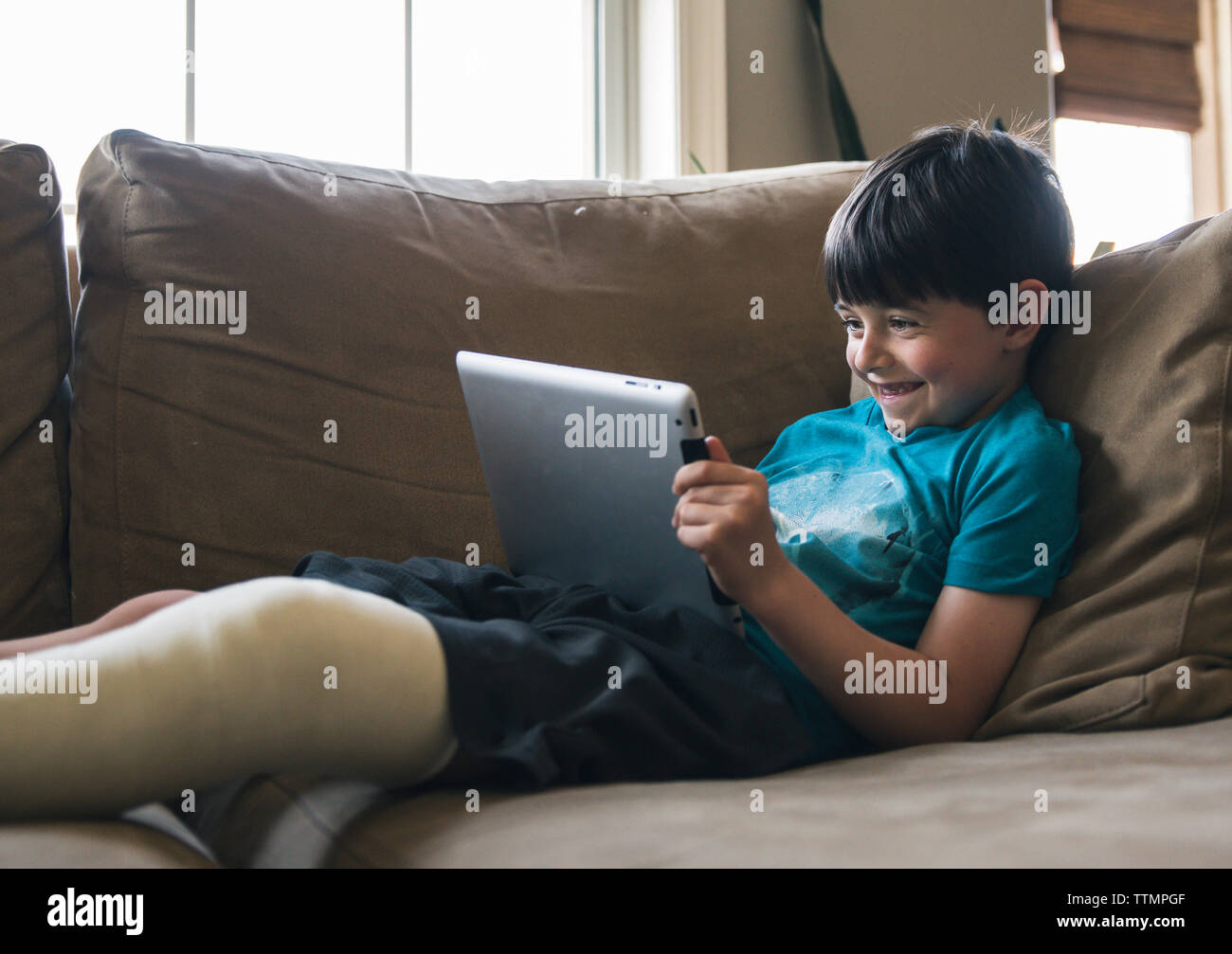 Smiling boy with fractured leg using tablet computer while lying on sofa at home Stock Photo