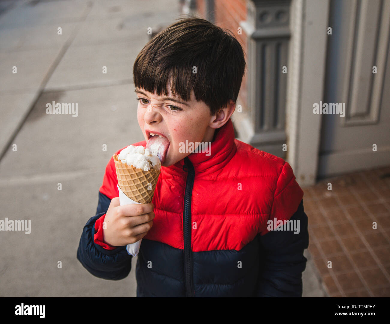 Boy looking away while licking ice cream on footpath in city Stock Photo