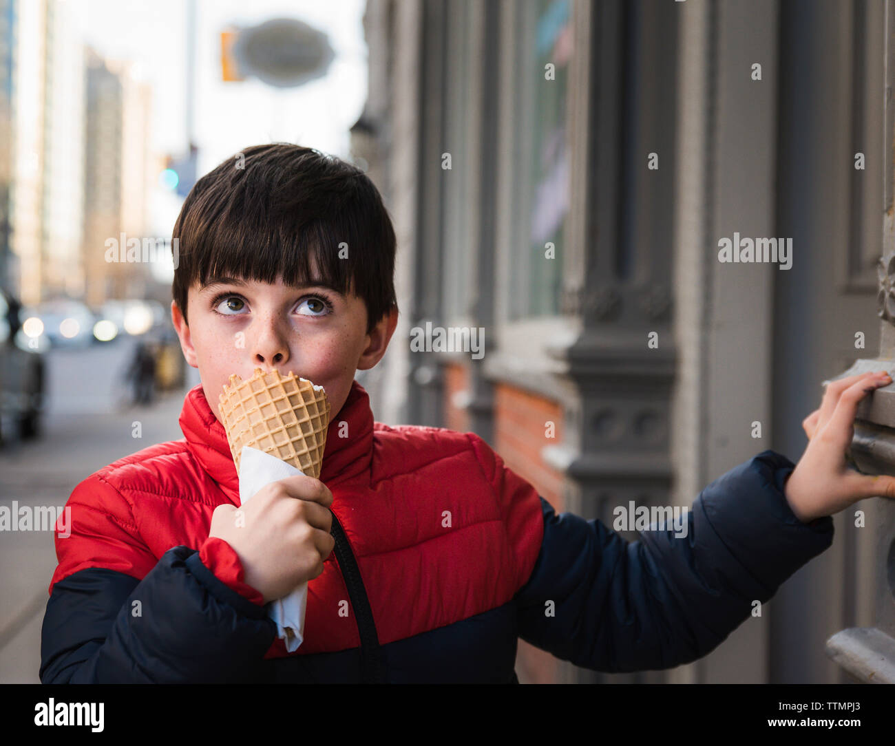 Boy looking up while eating ice cream on footpath in city Stock Photo