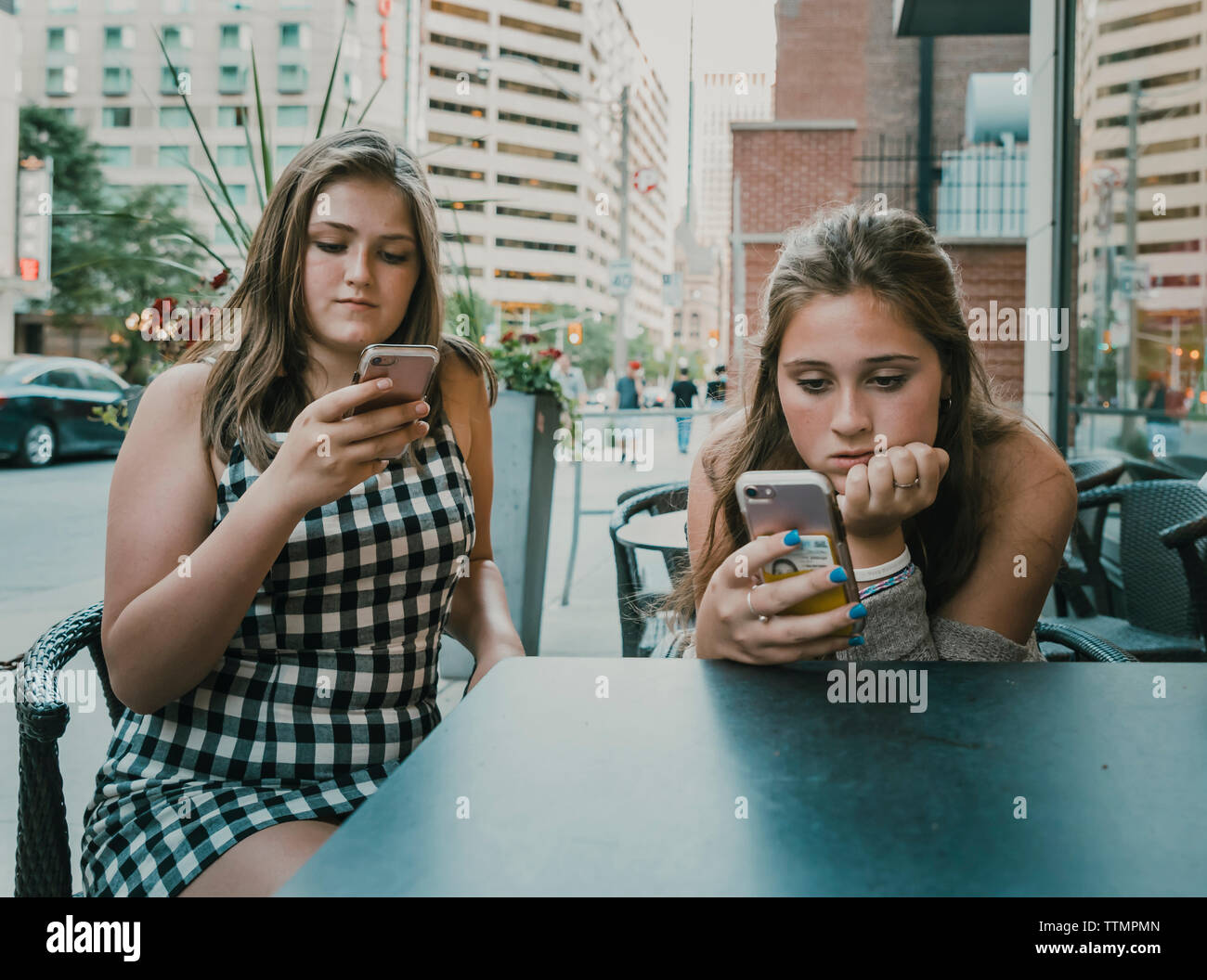 Female friends using smart phones while sitting at sidewalk cafe Stock Photo
