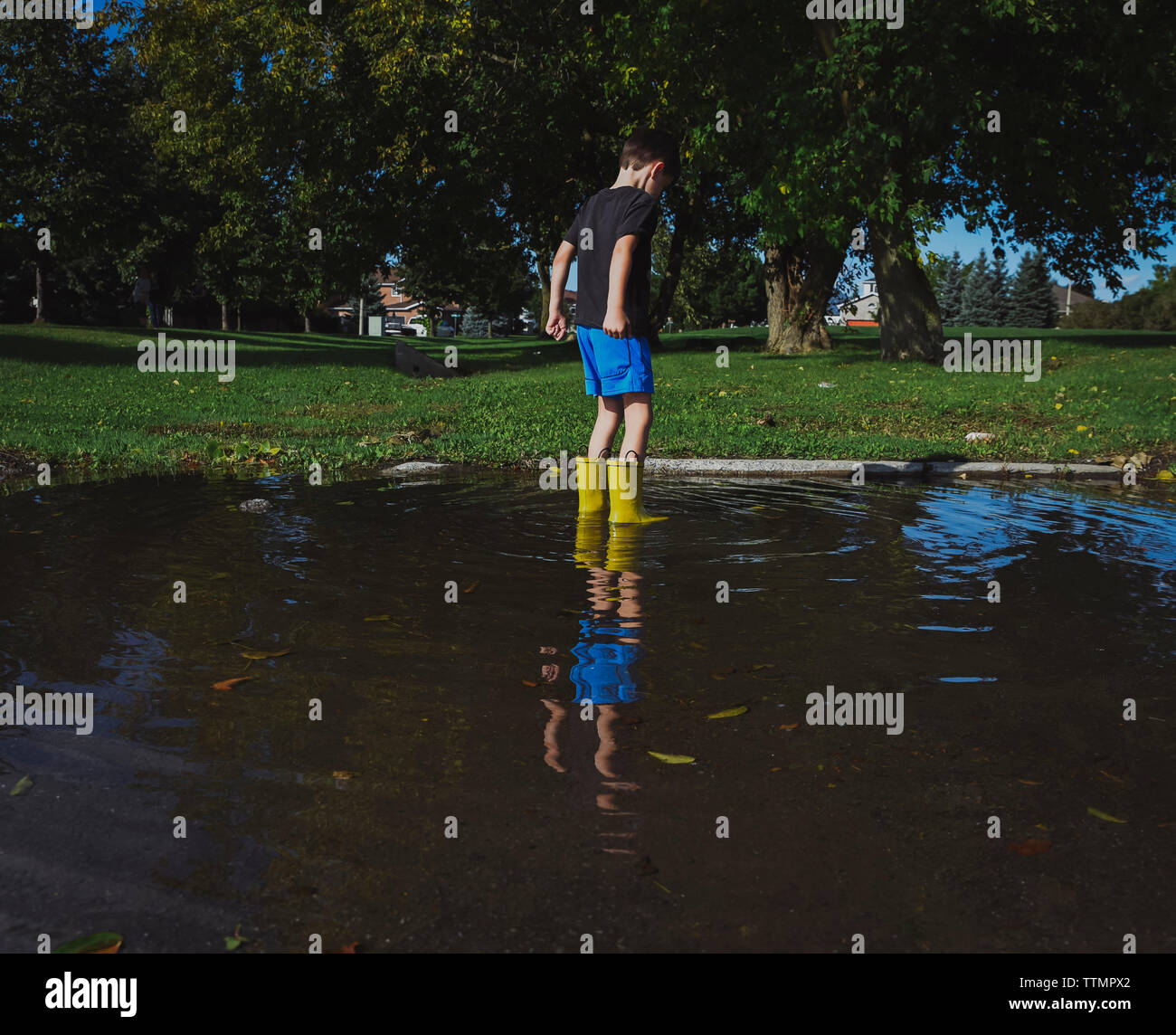 Playful boy wearing rubber boots standing in puddle at park Stock Photo