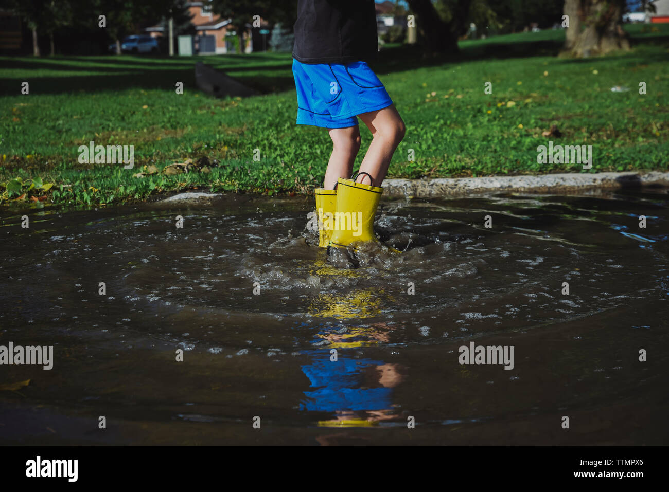 Low section of playful boy wearing rubber boots jumping in puddle at