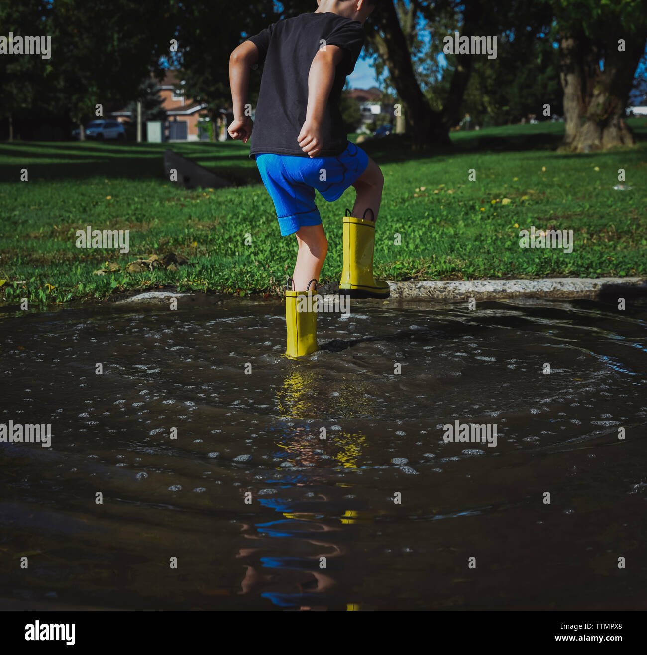 Rear view of playful boy stamping Foot while standing in puddle at park Stock Photo