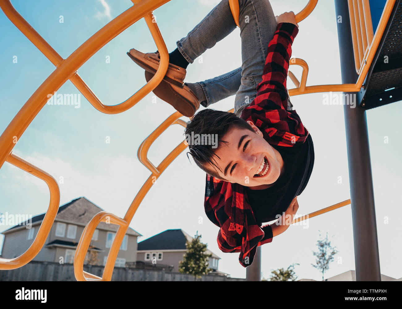 Portrait of carefree cheerful boy hanging from metallic steps at playground during summer Stock Photo