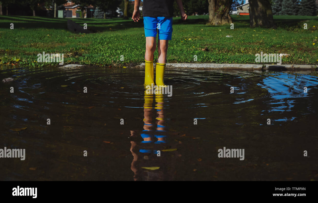 Low section of boy wearing rubber boots standing in puddle by field Stock Photo