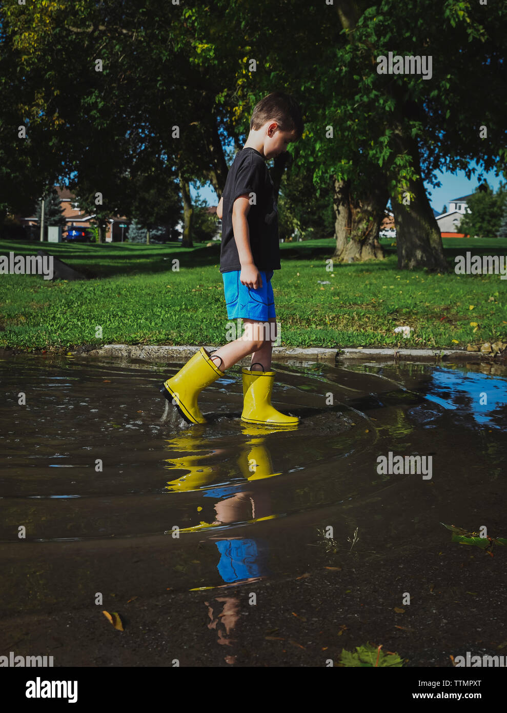 Full length of boy in rubber boots walking on puddle by trees Stock Photo