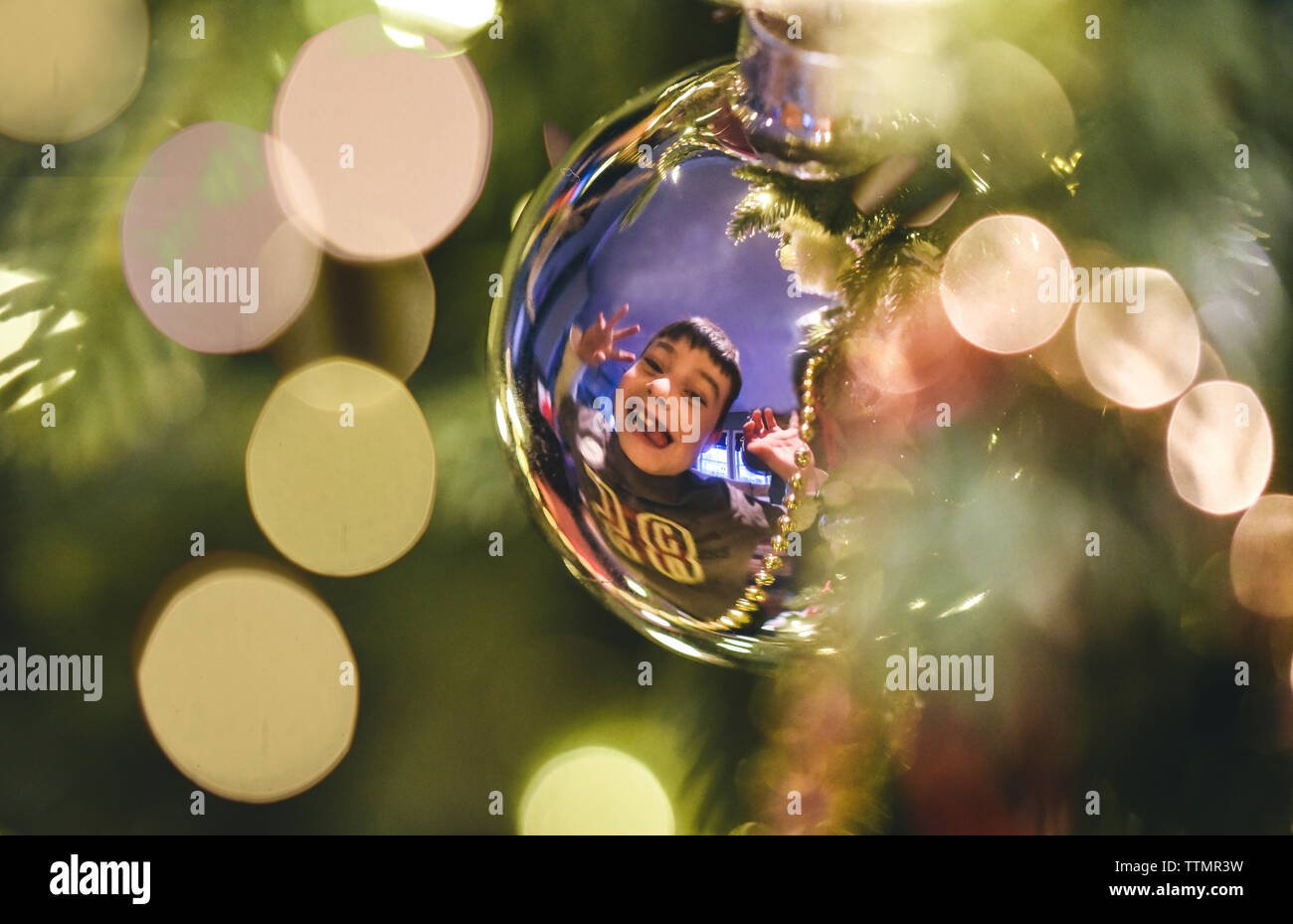 Reflection on silver Christmas ball of young boy making silly face. Stock Photo