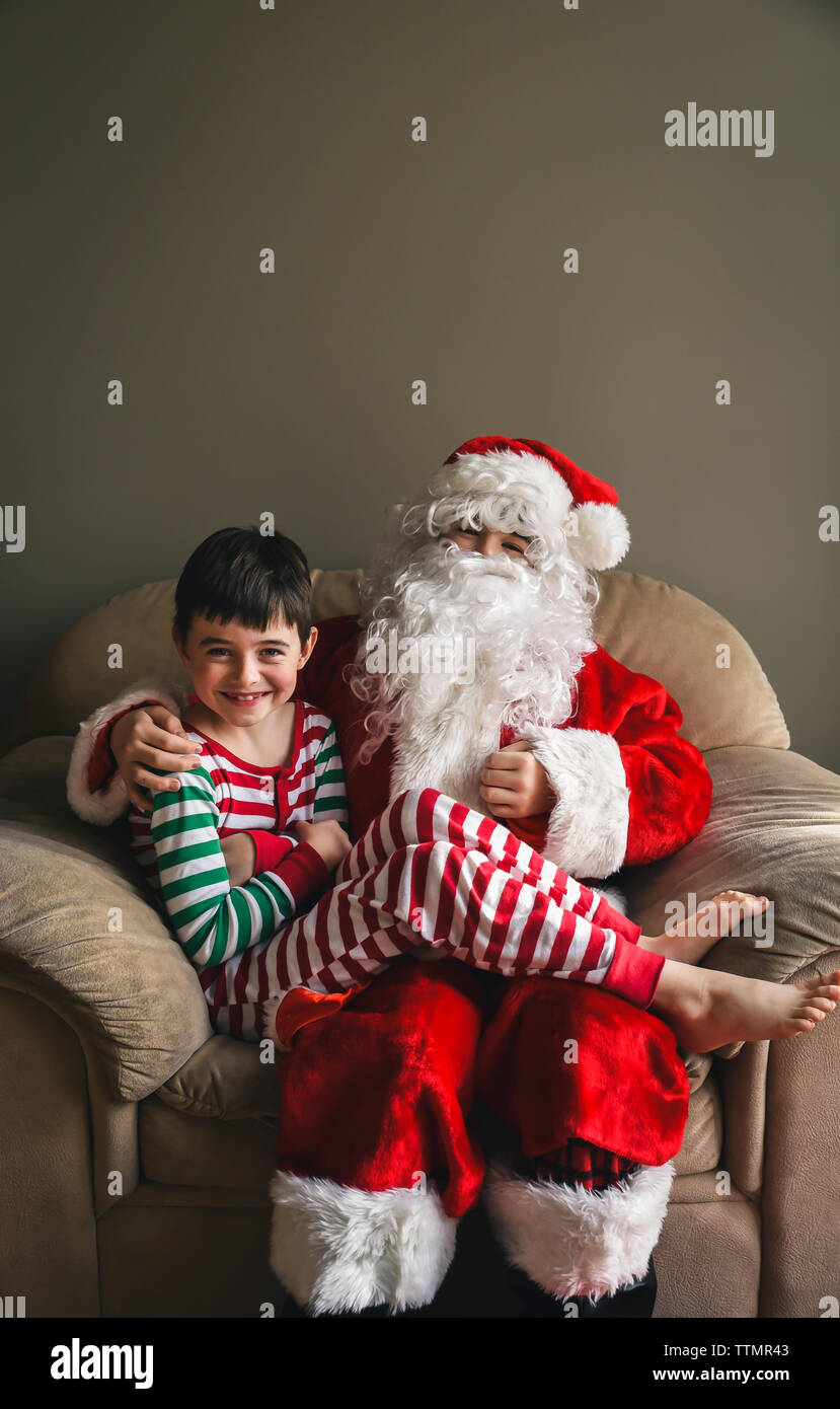Young boy in Christmas pyjamas smiling while sitting on Santa's lap. Stock Photo