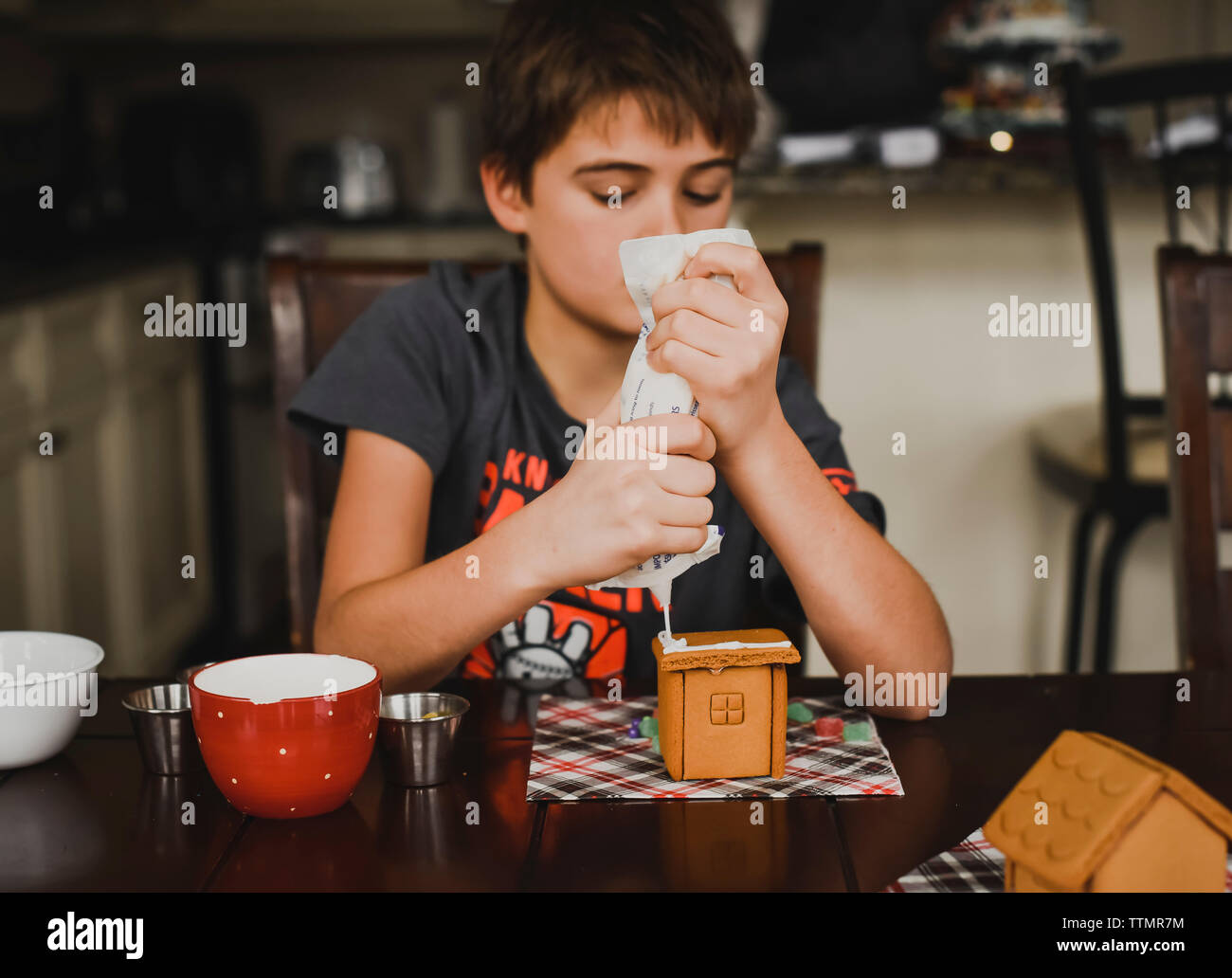 Adolescent boy putting icing on a gingerbread house. Stock Photo