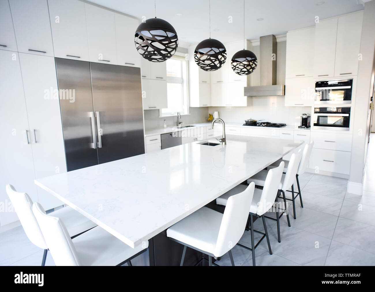 Modern white kitchen with large island and stainless steel appliances. Stock Photo
