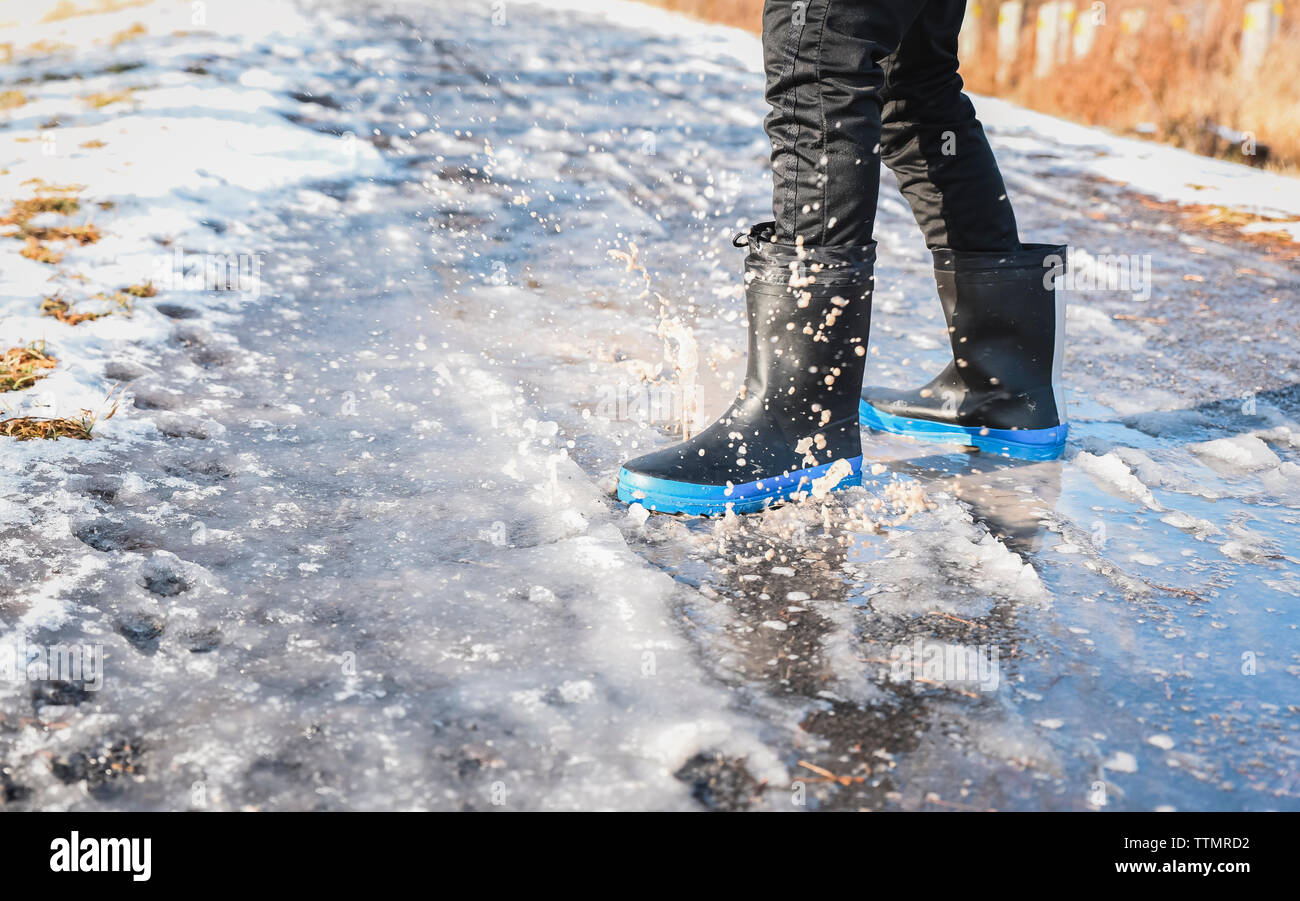 Cropped close up of rubber boots splashing in a slushy puddle. Stock Photo