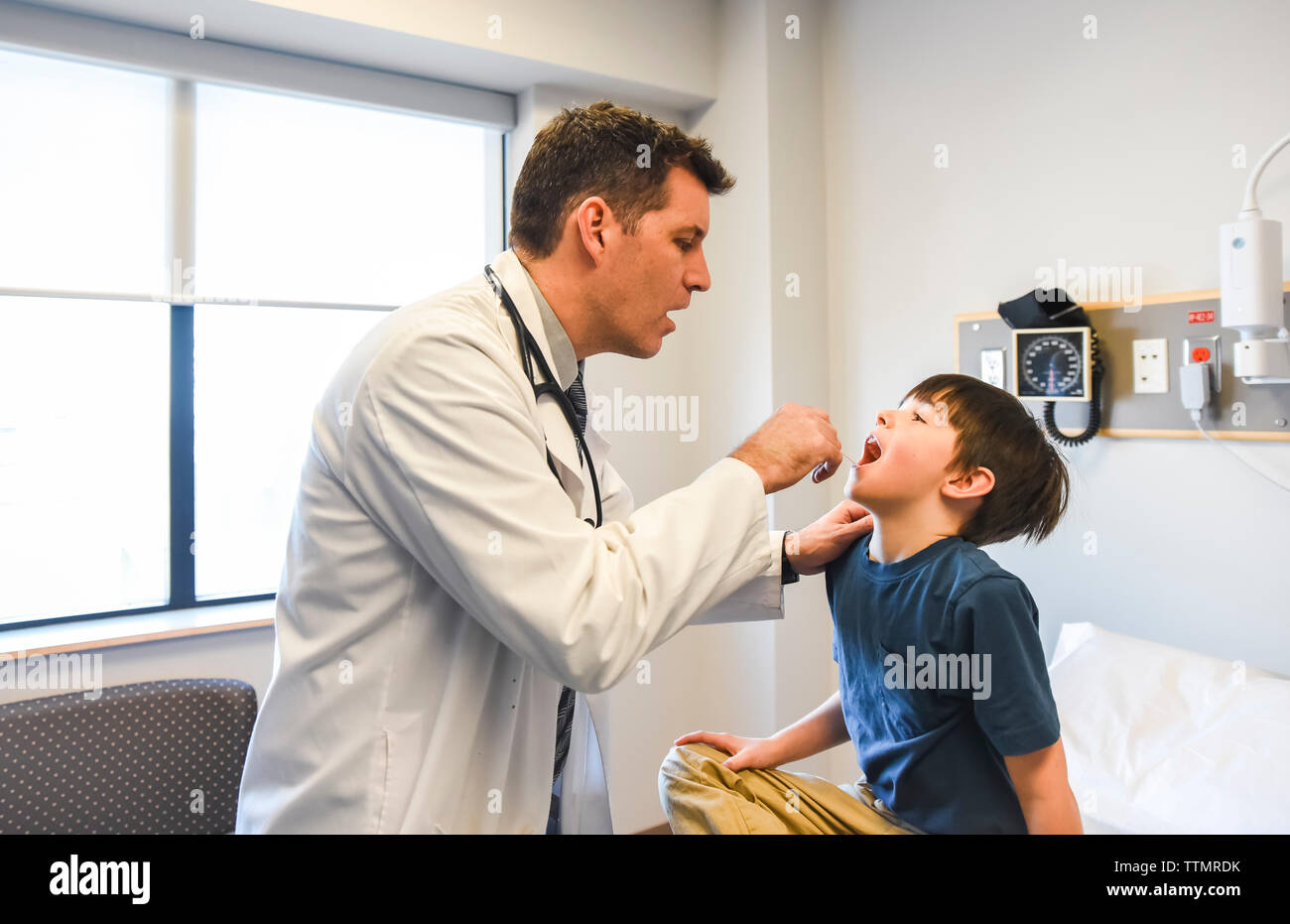 Doctor looking in the mouth of a young patient on exam table. Stock Photo