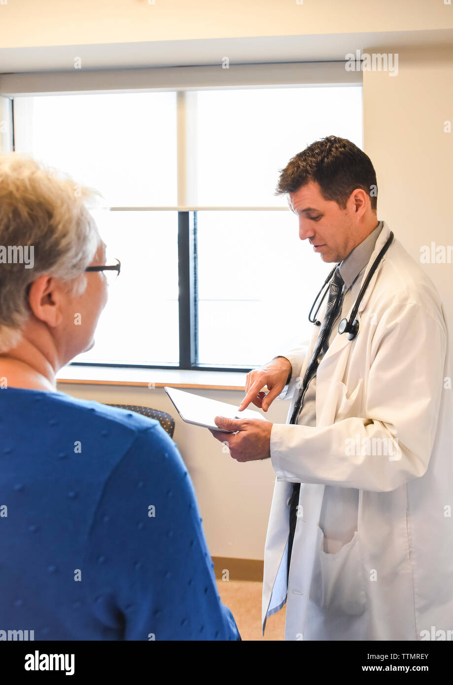 Doctor holding tablet speaking to older patient in a clinical setting. Stock Photo